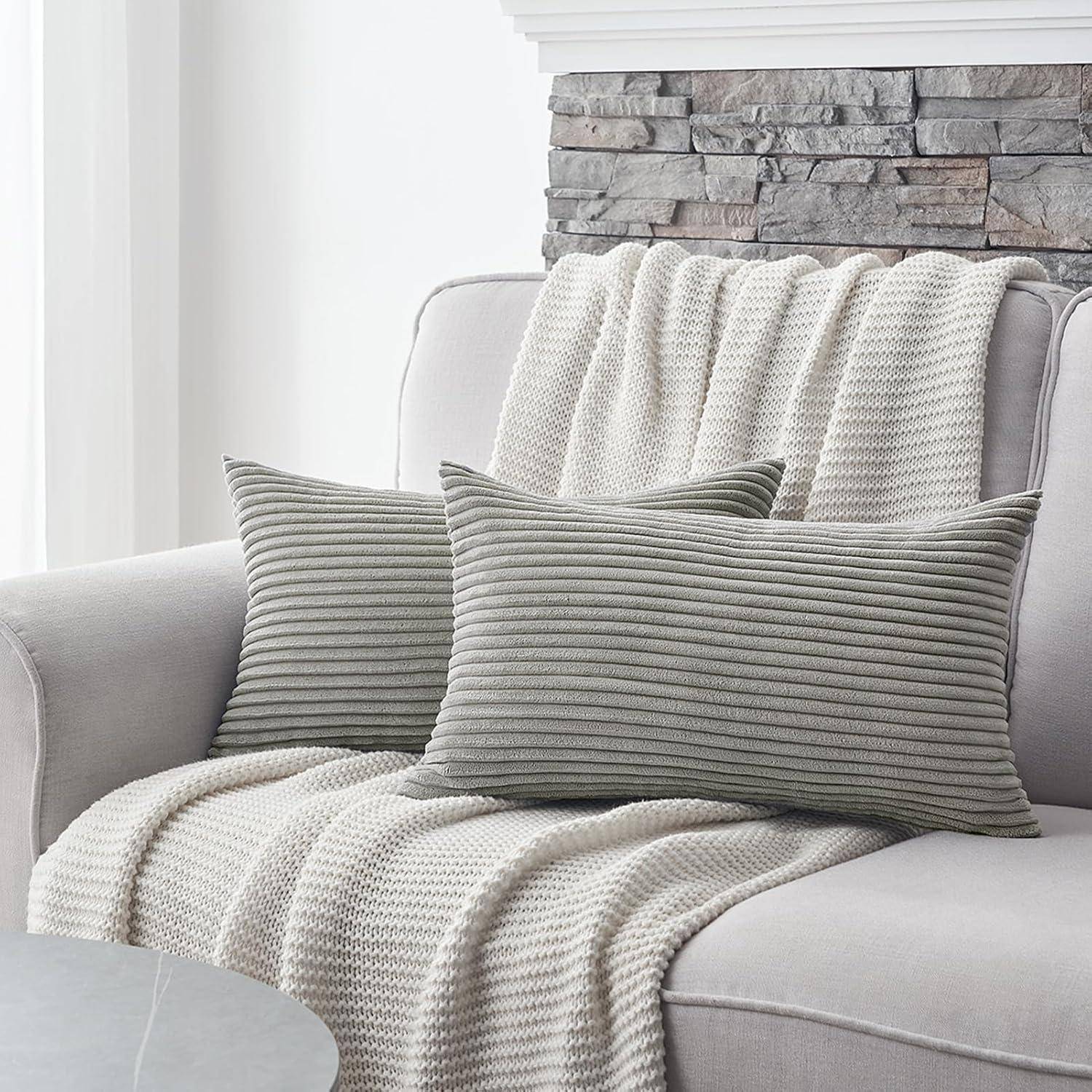 Ein gemütliches Wohnzimmer präsentiert ein hellgraues Sofa mit einer strukturierten Decke und zwei gestreiften Kissen, vor einer Steinwandhintergrund.