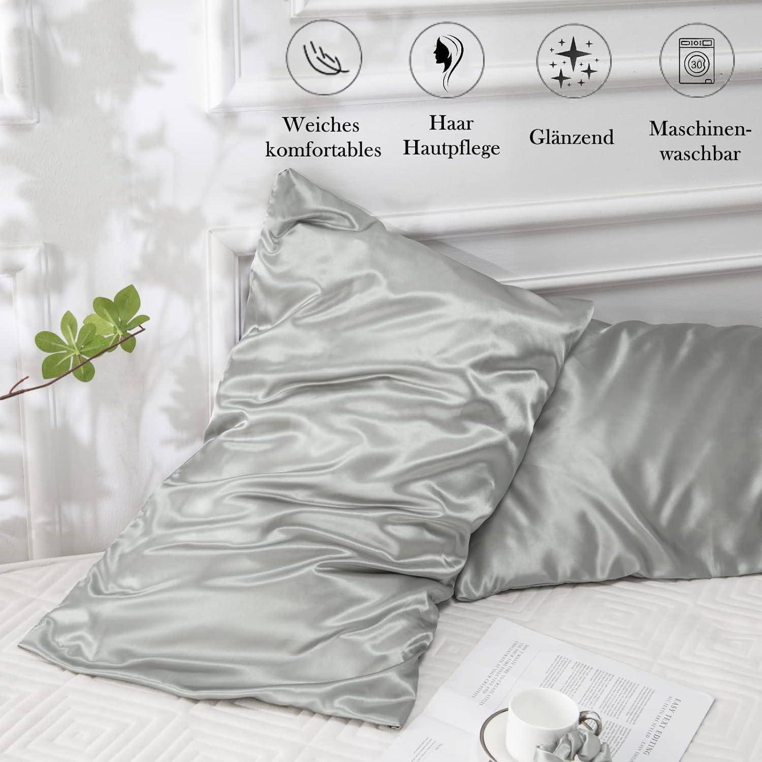 Silberne Satin-Kissenbezüge auf einem Bett mit Symbolen, die Eigenschaften anzeigen: weiche Bequemlichkeit, Haarpflege, glänzend und maschinell waschbar.