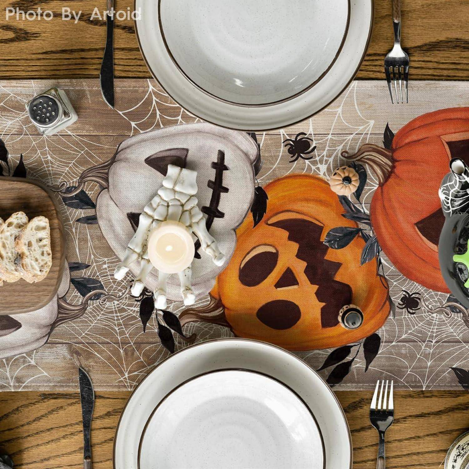 Eine Tischgedekoration mit Halloween-Motiven, einschließlich Kürbisse mit bemalten Gesichtern, Spinnwebmustern und einer brennenden Kerze.