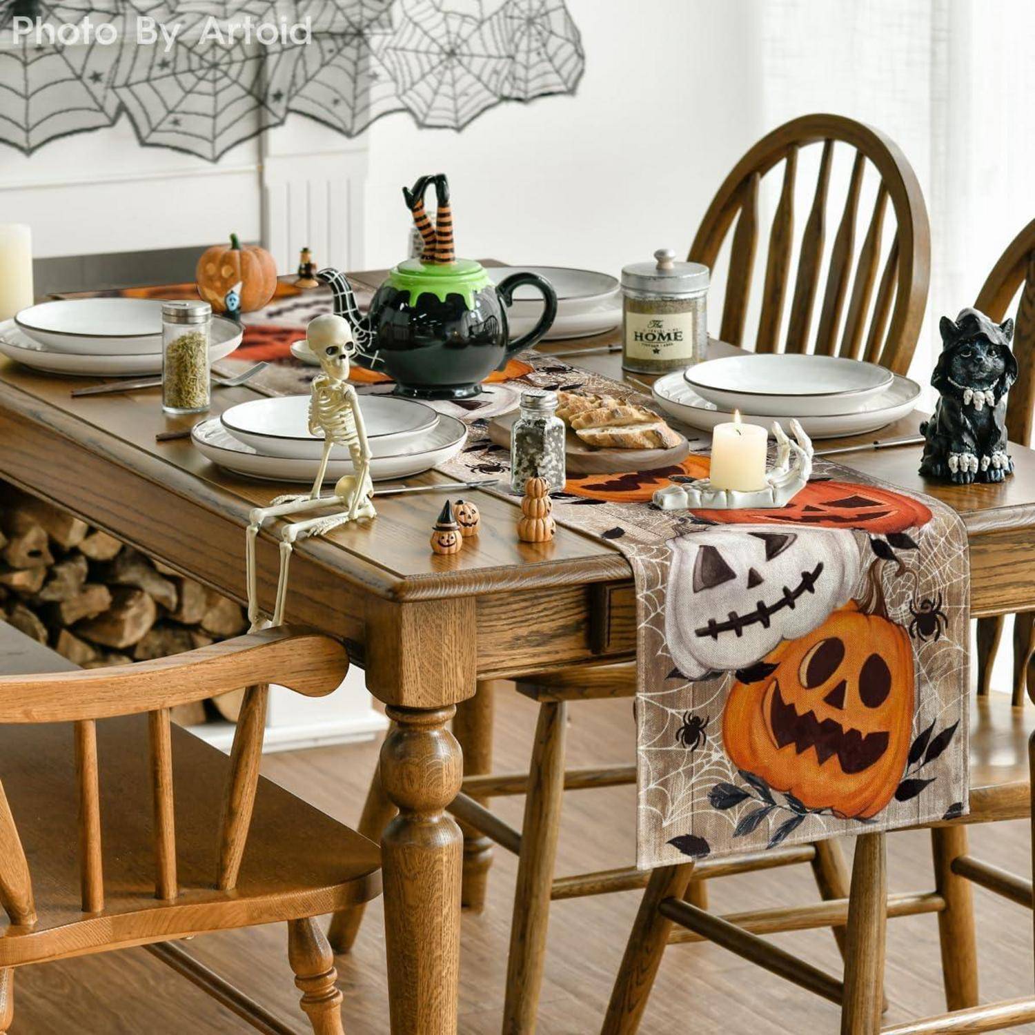 Ein Esstisch, festlich für Halloween dekoriert, mit Herbst-Motiven, einschließlich Kürbisdesigns und einem kleinen Skelett. Kerzen und thematische Teller sind vorhanden.