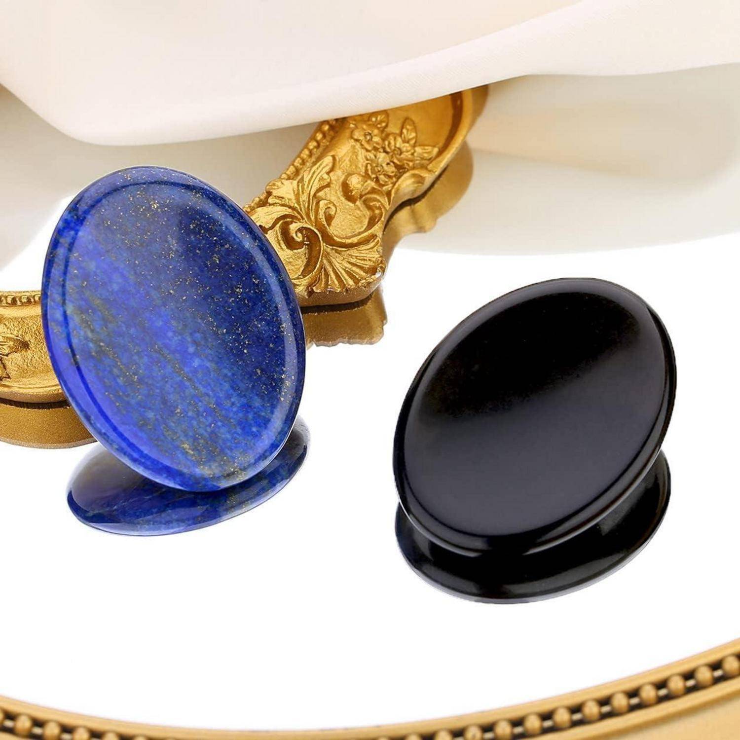 Zwei dekorative Pop-Socket-Griffe: einer mit blauer Steintextur und ein anderer in solidem Schwarz, auf einer reflektierenden Oberfläche platziert.