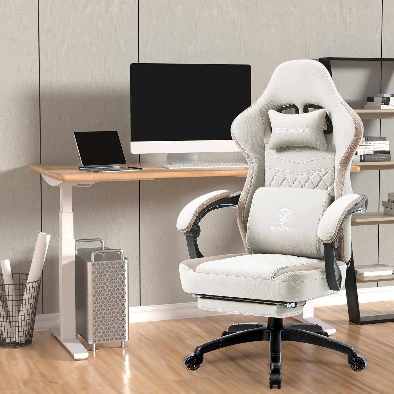 Ein weißer Gaming-Stuhl mit grauen Akzenten steht vor einem Holzschreibtisch mit einem Computermonitor und Büchern in einem ordentlichen Büroraum.