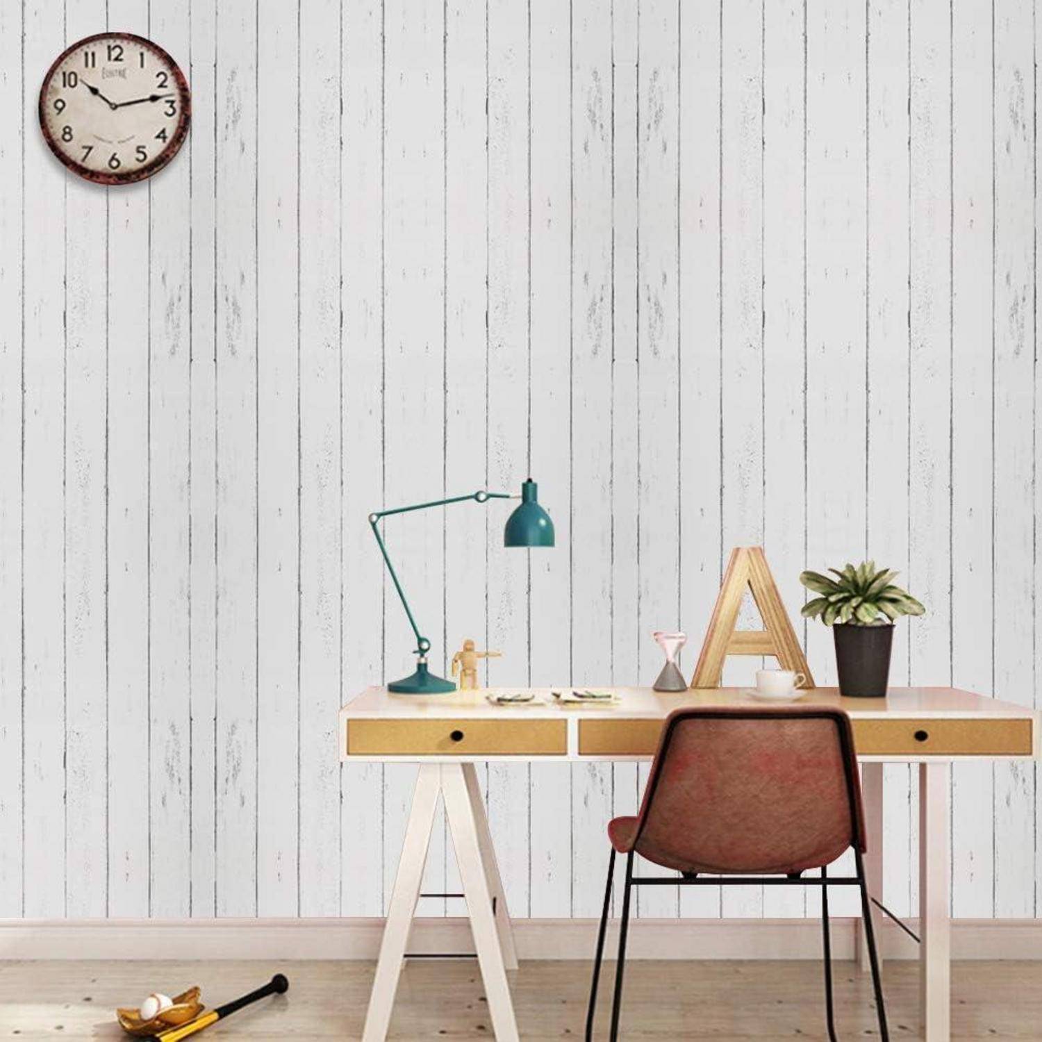 Ein minimalistischer Arbeitsplatz mit einem Holzschreibtisch, einer Lampe, einer Pflanze, einem Stuhl und einer Uhr an einer weißen Vertäfelung. Eine Violine liegt auf dem Boden.