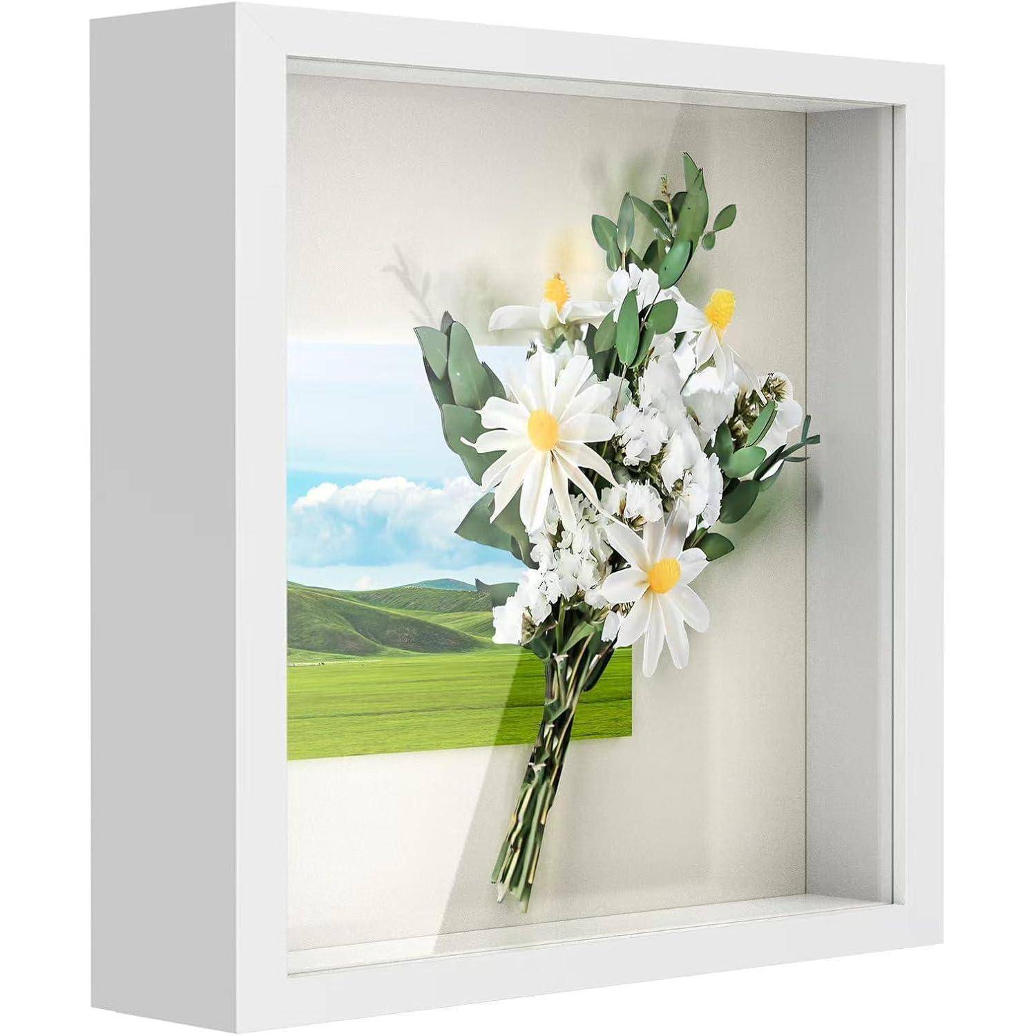 Ein Blumenstrauß aus weißen Gänseblümchen und Grünzeug in einem Schattenrahmen vor einer malerischen Kulisse von sanft geschwungenen grünen Hügeln unter einem blauen Himmel.