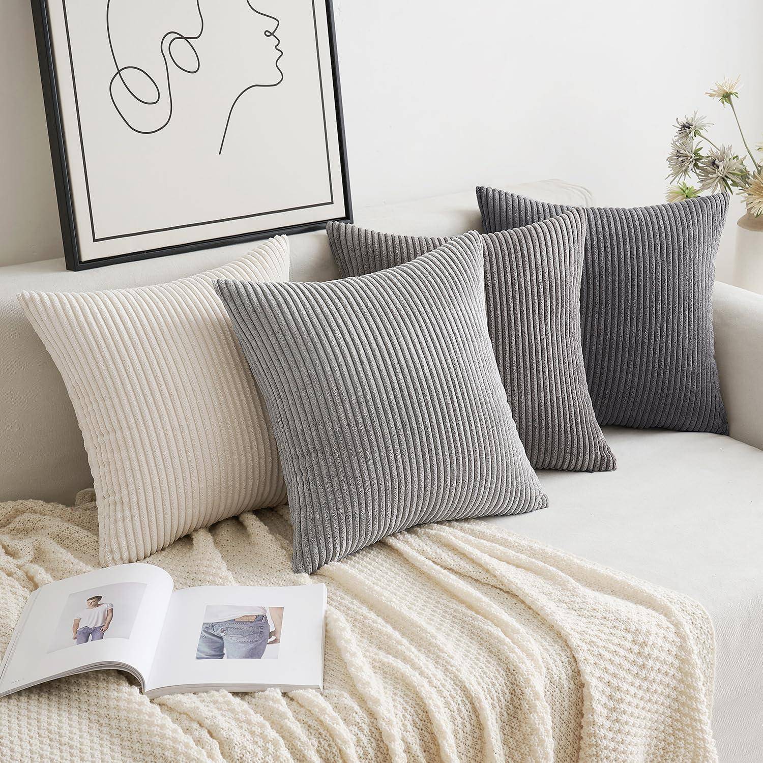 Ein beige Sofa mit strukturierten Kissen in Weiß, Grau und Dunkelgrau, ein Linienkunst-Porträt an der Wand darüber und ein aufgeschlagenes Buch auf einem gestrickten Überwurf.