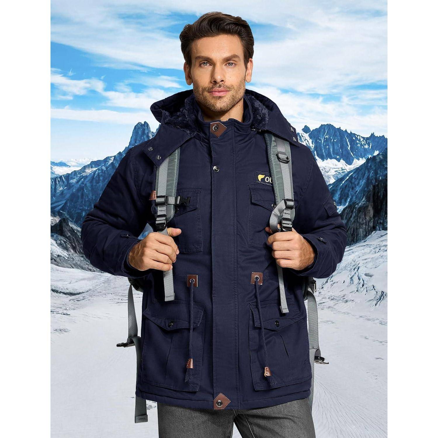 Ein Mann in einer marineblauen Jacke und mit einem Rucksack steht in einer verschneiten Berglandschaft und blickt direkt in die Kamera.