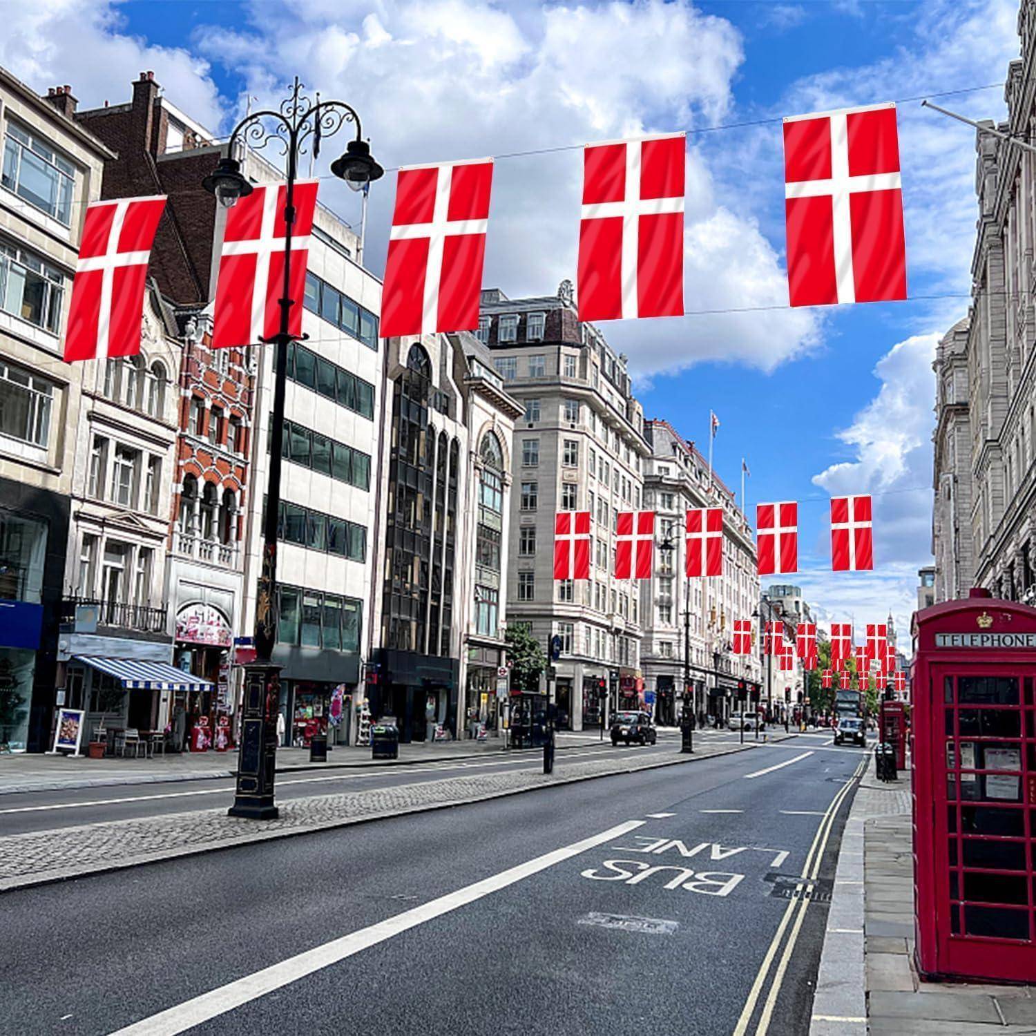 Eine Stadtstraße gesäumt von historischen Gebäuden, dänische Flaggen zwischen den Häusern aufgehängt, und eine rote Telefonzelle auf dem Gehweg unter einem blauen Himmel.
