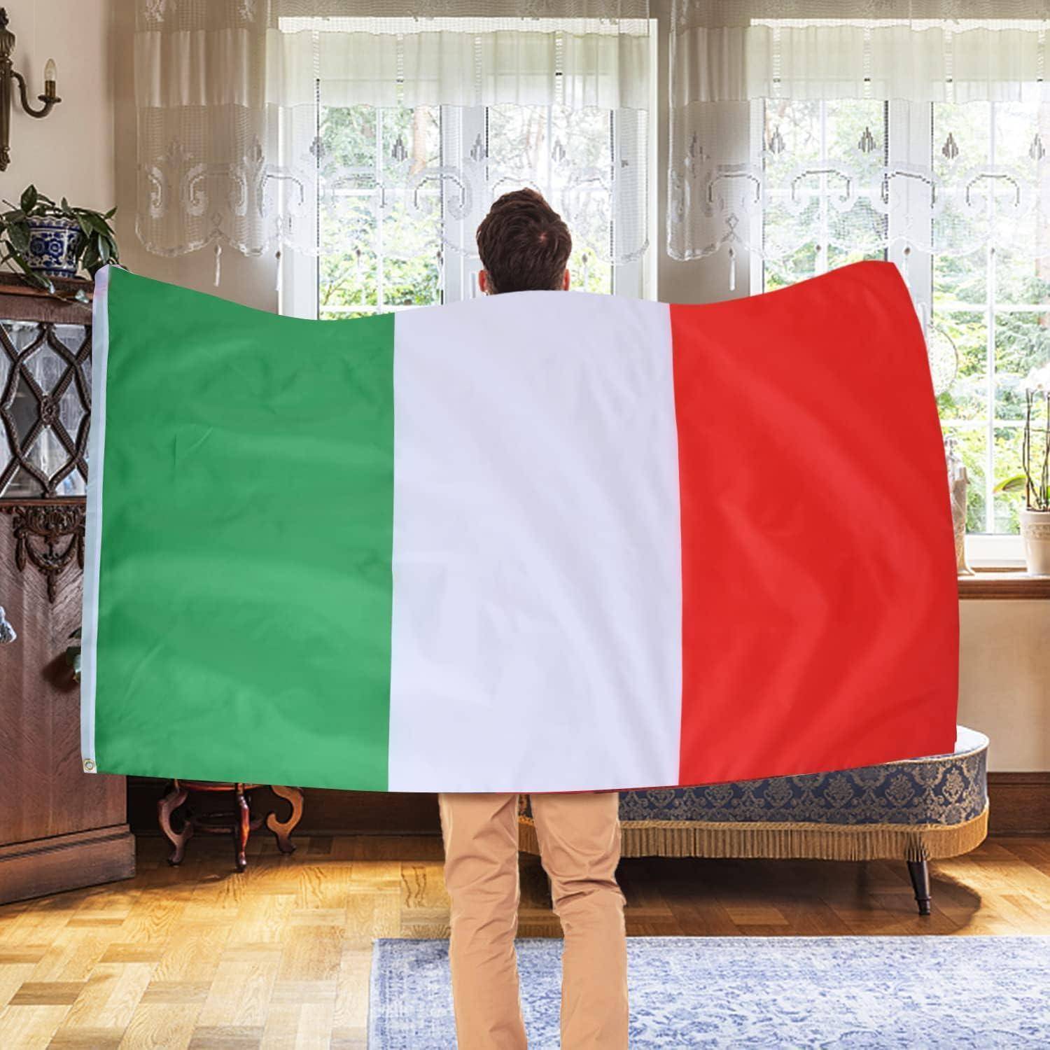 Eine Person steht drinnen und hält eine große italienische Flagge mit vertikalen grünen, weißen und roten Streifen vor einem Fenster.