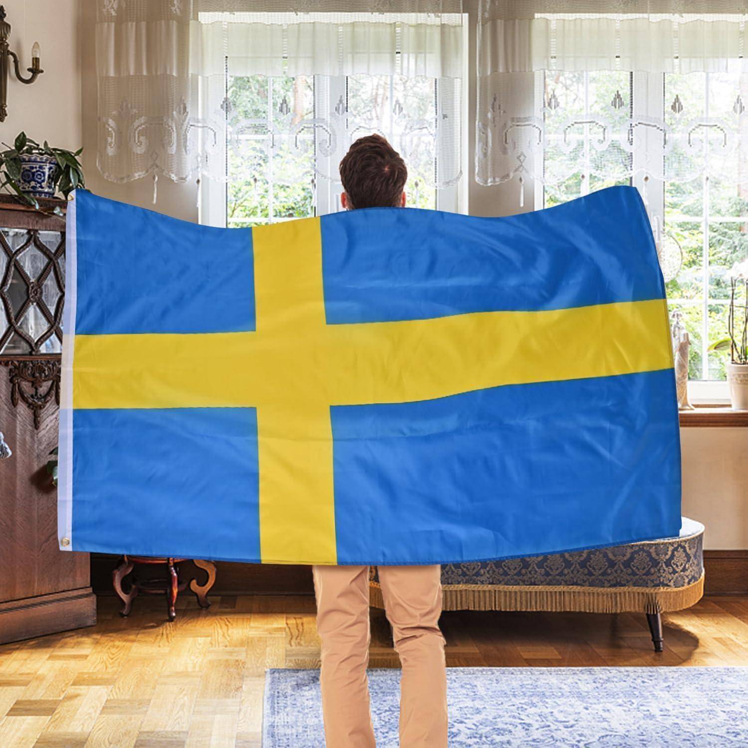 Eine Person steht drinnen und hält eine große schwedische Flagge, wobei der Raum traditionelle Einrichtung und ein Fenster im Hintergrund aufweist.