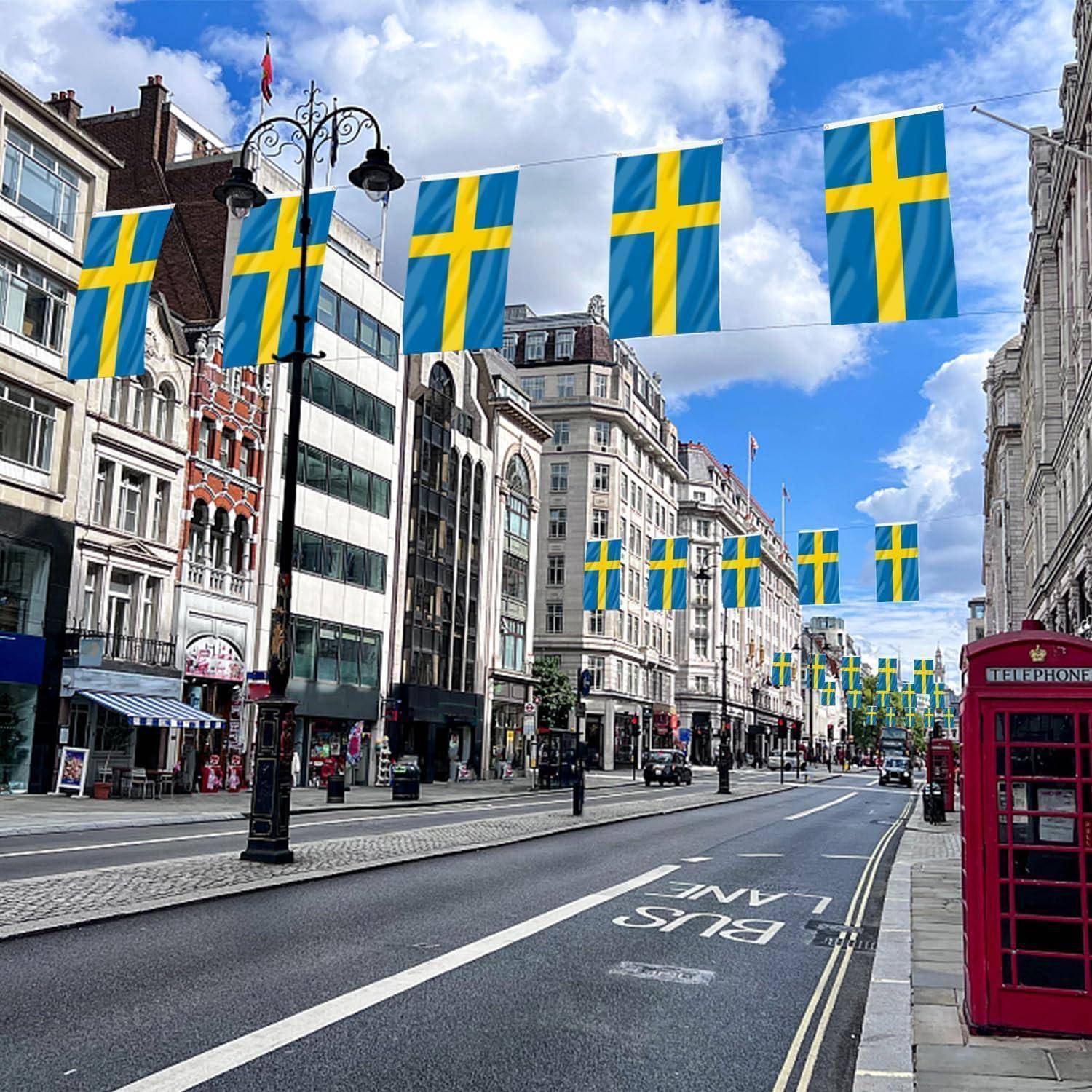 Eine Stadtstraße mit schwedischen Flaggen, die über den Straßen hängen, umgeben von historischen Gebäuden. Eine rote Telefonzelle steht auf dem Gehweg.