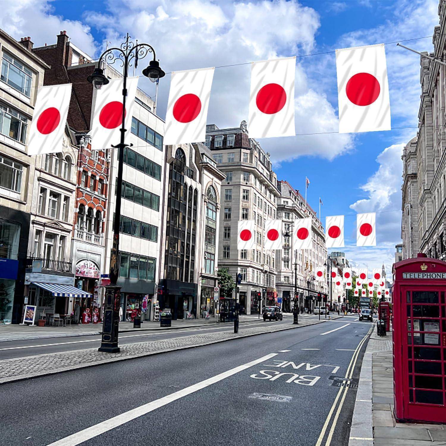 Eine Straße in einer Stadt ist mit weißen Flaggen geschmückt, die rote Kreise tragen und der japanischen Flagge ähneln, rechts daneben eine klassische rote Telefonzelle.