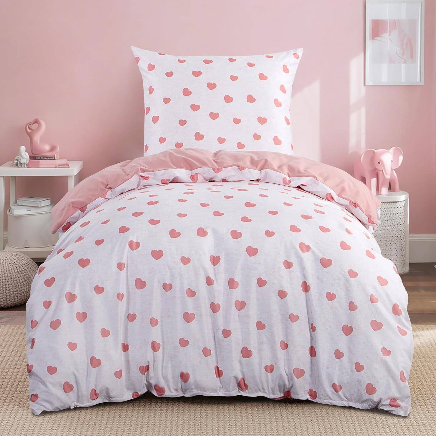 Ein gemütliches Schlafzimmer mit einer Bettwäsche mit Herzmuster auf einem Bett, umgeben von rosa Dekoration, die eine warme und einladende Atmosphäre schafft.