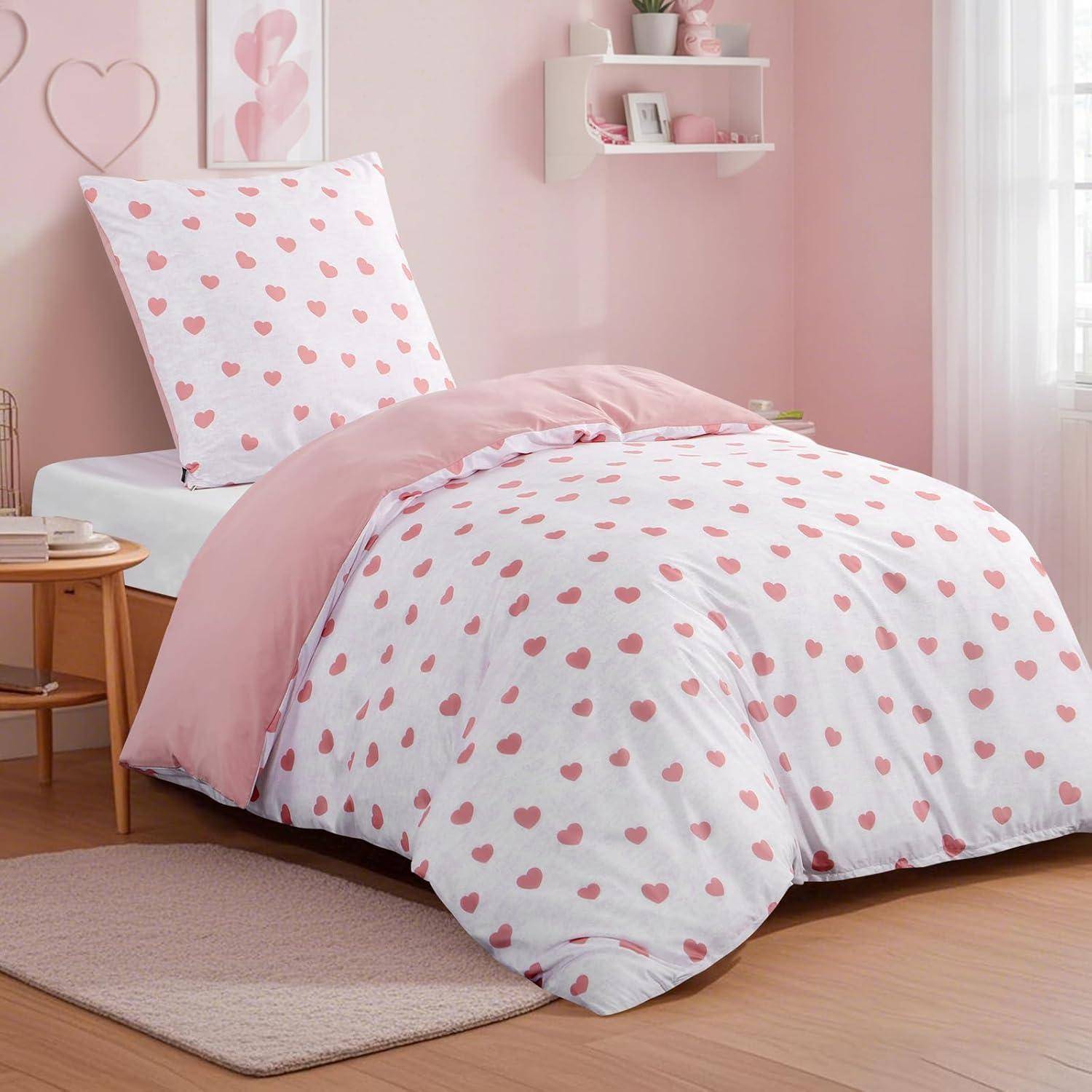 Ein gemütliches Schlafzimmer mit einer weißen Bettdecke, die mit rosa Herzen verziert ist, passendem Kissen, hellem Holzmobiliar und herzförmiger Wanddekoration.