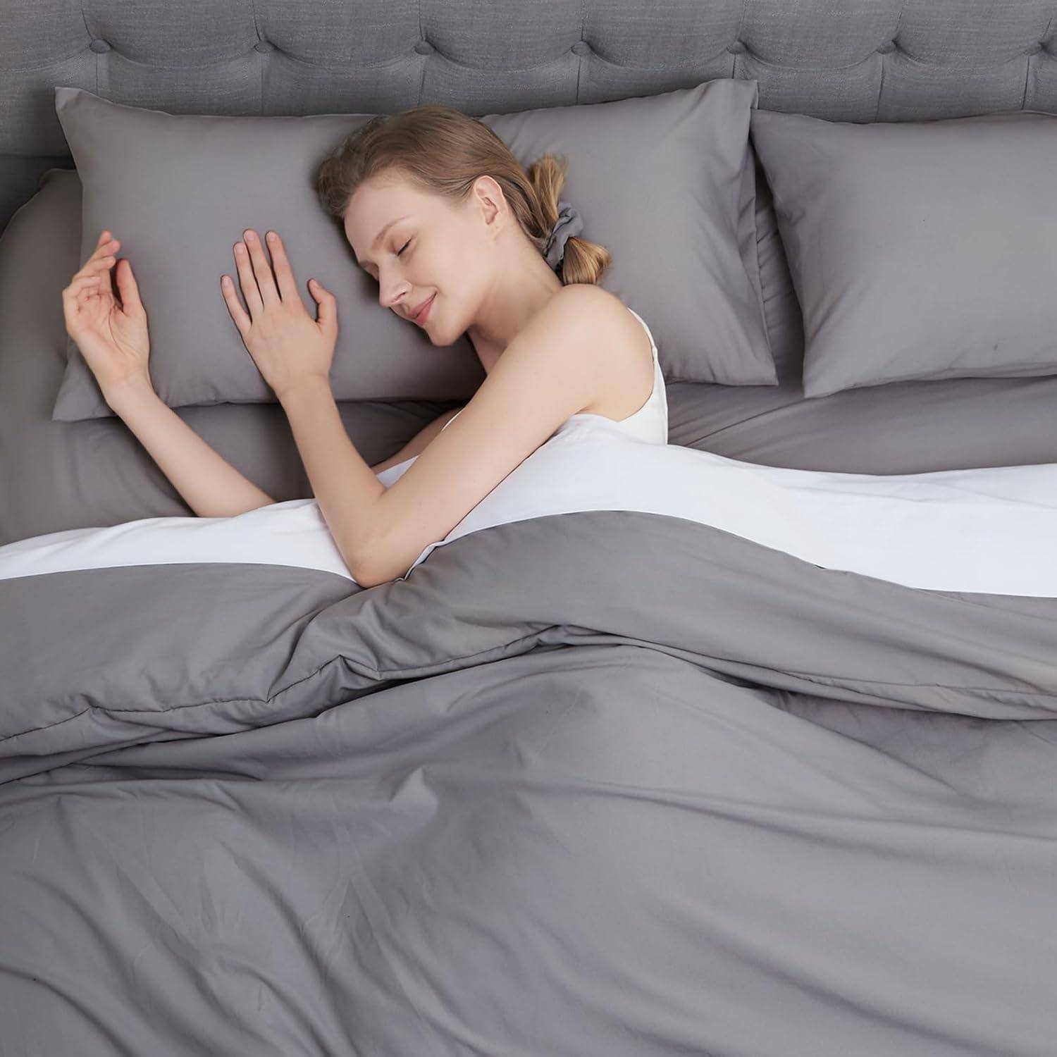 Eine Person liegt friedlich auf einem Bett mit grauen Laken und Kissen, lächelt sanft und vermittelt ein Gefühl von Komfort und Entspannung.