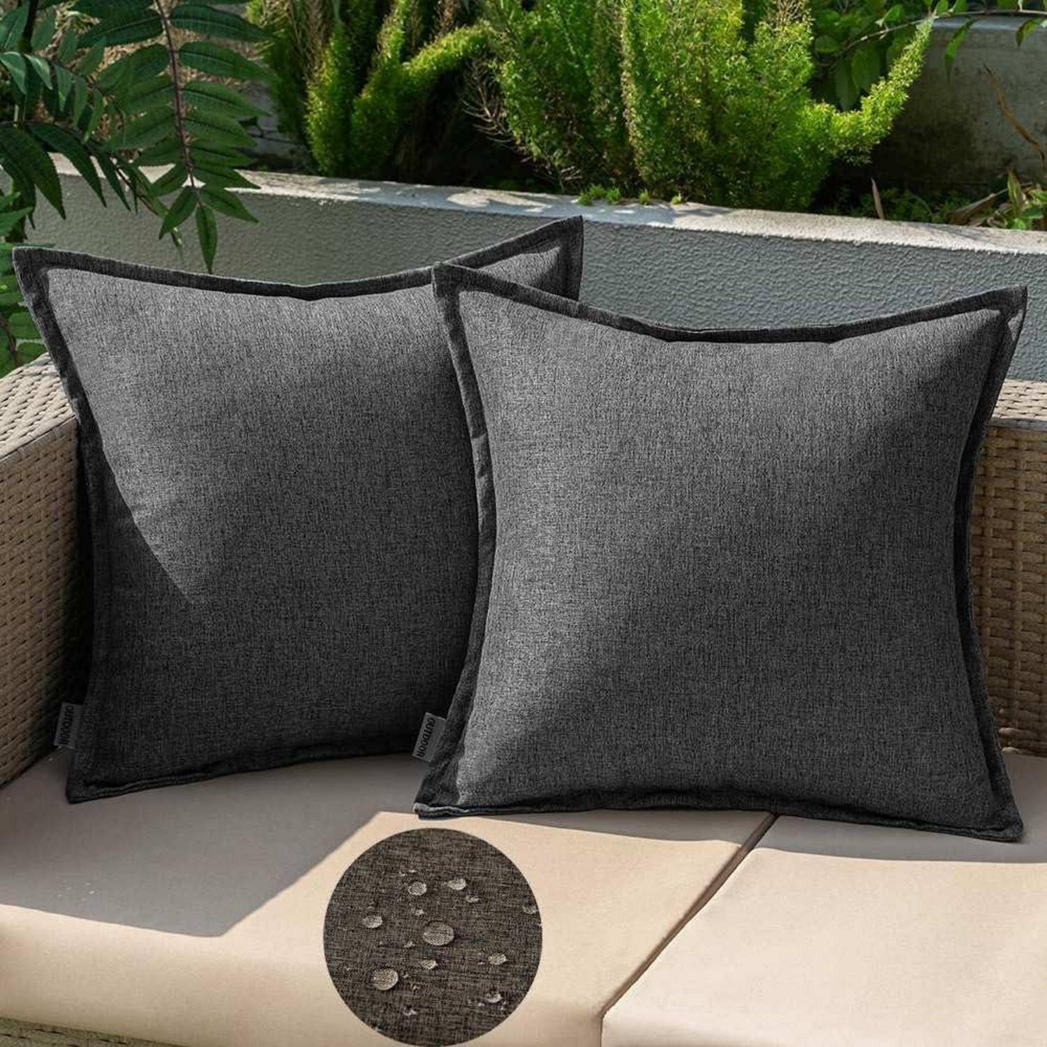 Zwei dunkelgraue Outdoor-Kissen auf einem beigen Sofa in einer Gartenumgebung. Eine Nahaufnahme zeigt die wasserabweisende Eigenschaft des Stoffes.