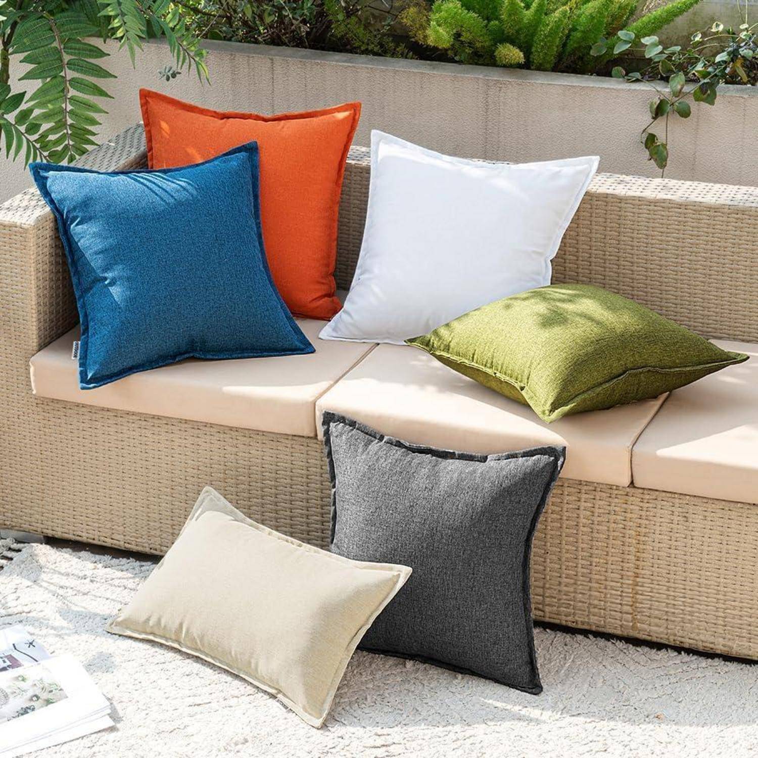 Outdoor-Terrasse mit einem beigen Rattansofa, geschmückt mit bunten Kissen in Orange, Blau, Weiß und Grün. Ein Kissen liegt auf dem Boden.