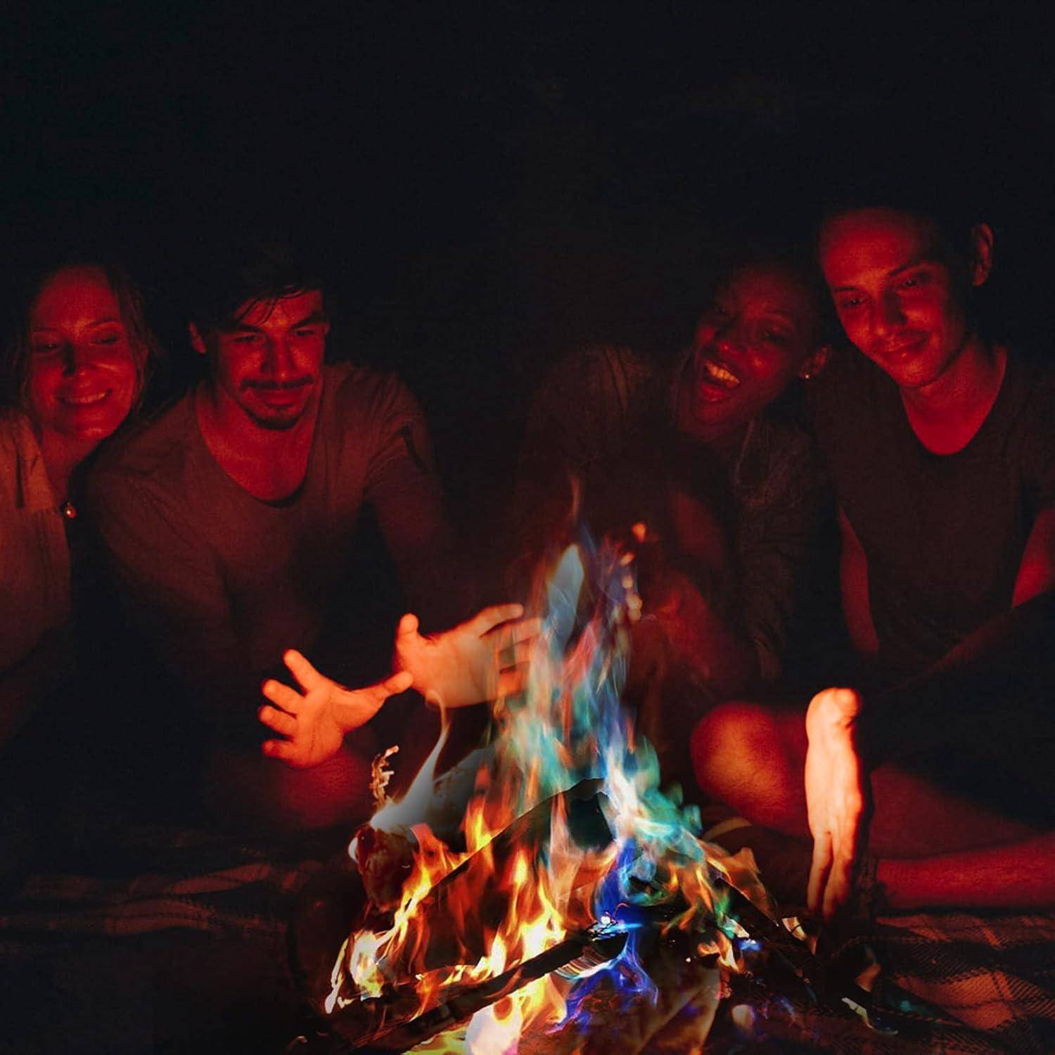 Eine Gruppe von vier Menschen sitzt dicht beieinander um ein lebhaftes Lagerfeuer, lächelt und genießt die Wärme in einer dunklen Outdoor-Umgebung.