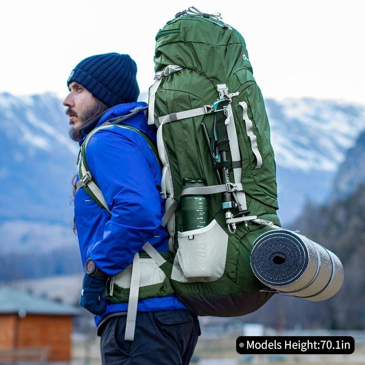 Eine Person trägt eine blaue Jacke und eine Mütze und hat einen großen grünen Wanderrucksack mit Campingausrüstung, während sie im Freien mit Bergen im Hintergrund steht.