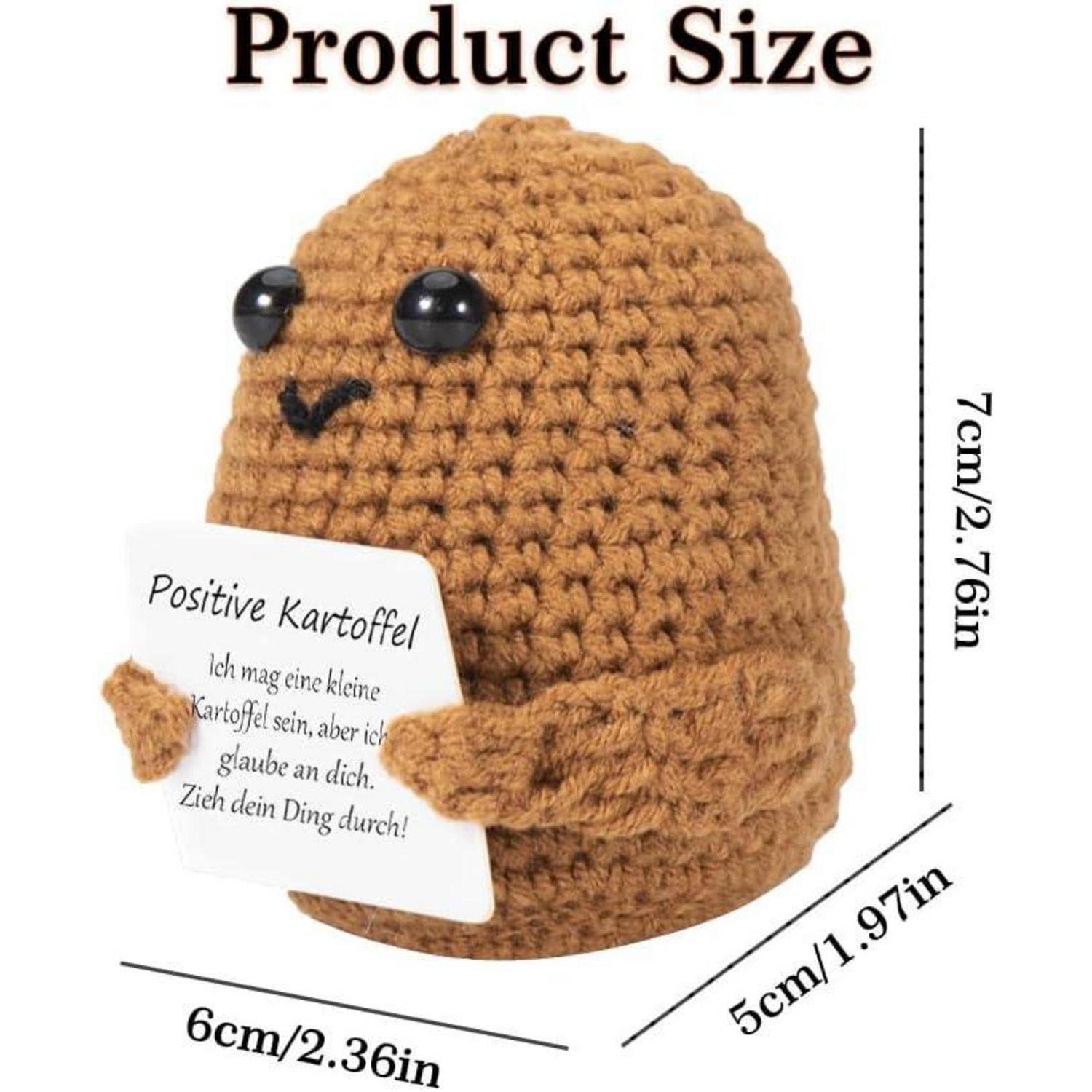 Gehäkelte Kartoffelfigur, die ein Schild hält. Abmessungen: 7 cm hoch, 6 cm breit, 5 cm tief. Das Schild auf Deutsch lautet 