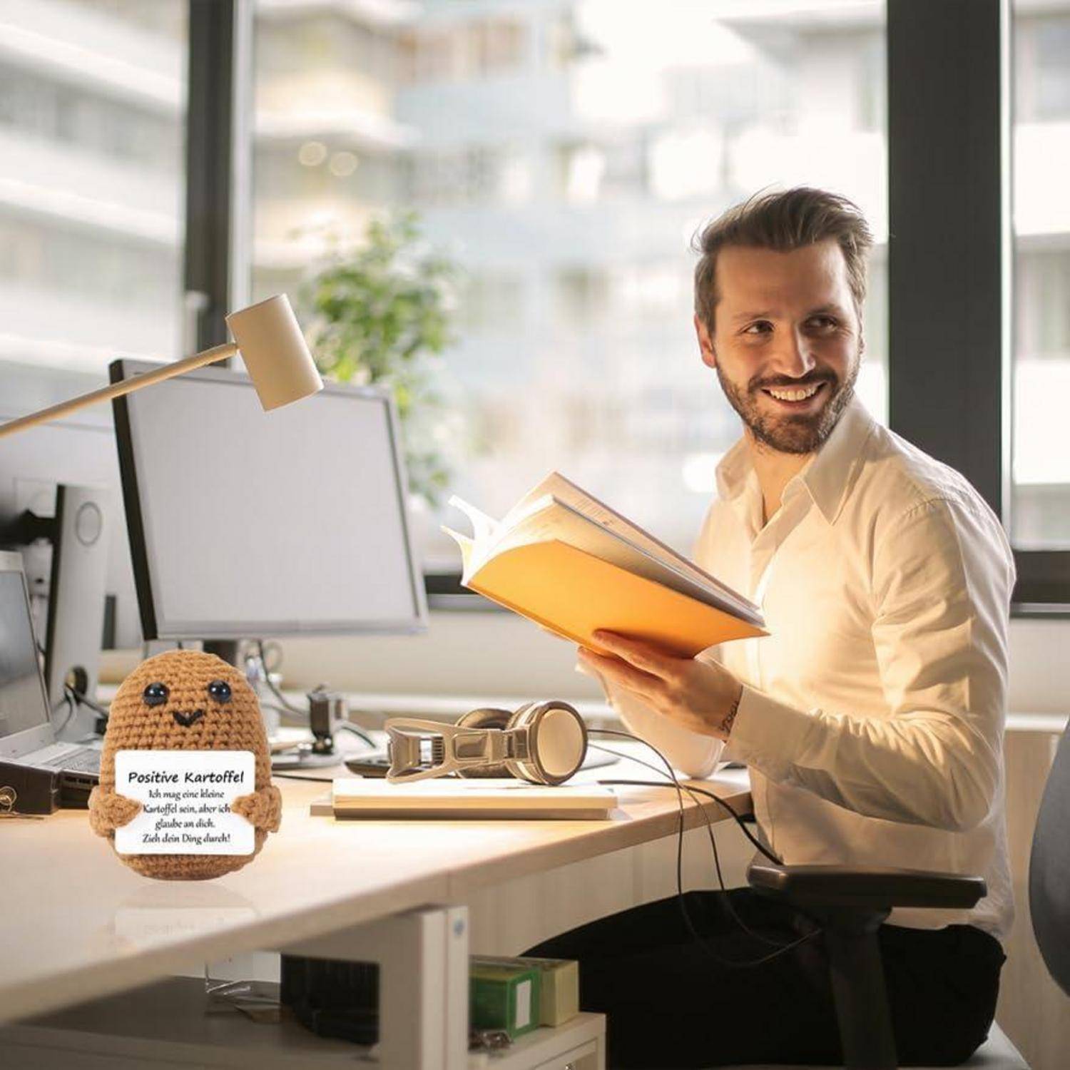 Eine Person, die lächelt, während sie ein Buch an einem hellen, modernen Büroschreibtisch liest; ein Plüschtier mit dem Text 