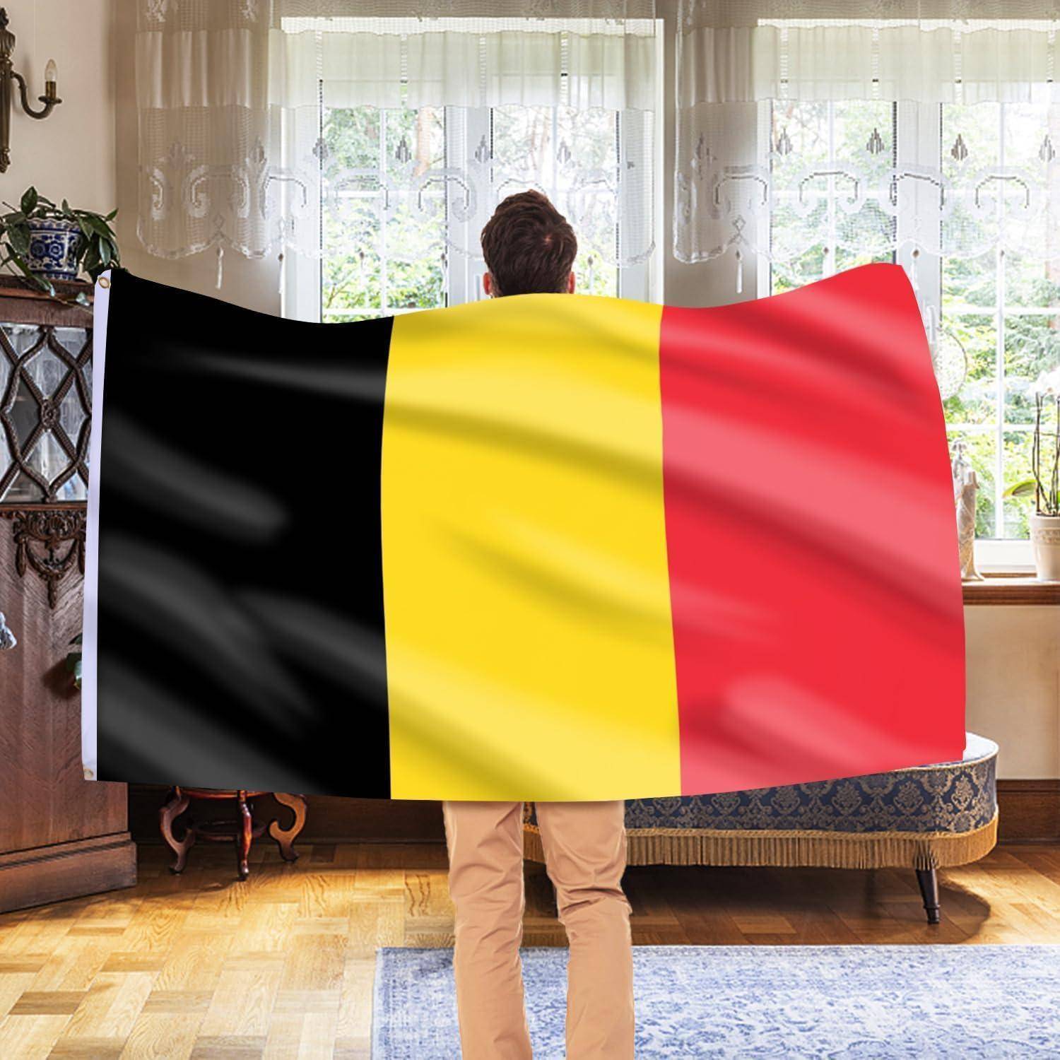 Eine Person hält eine große belgische Flagge in Innenräumen und verdeckt dabei teilweise ihr Sichtfeld. Natürliches Licht fällt durch dekorative Vorhänge.