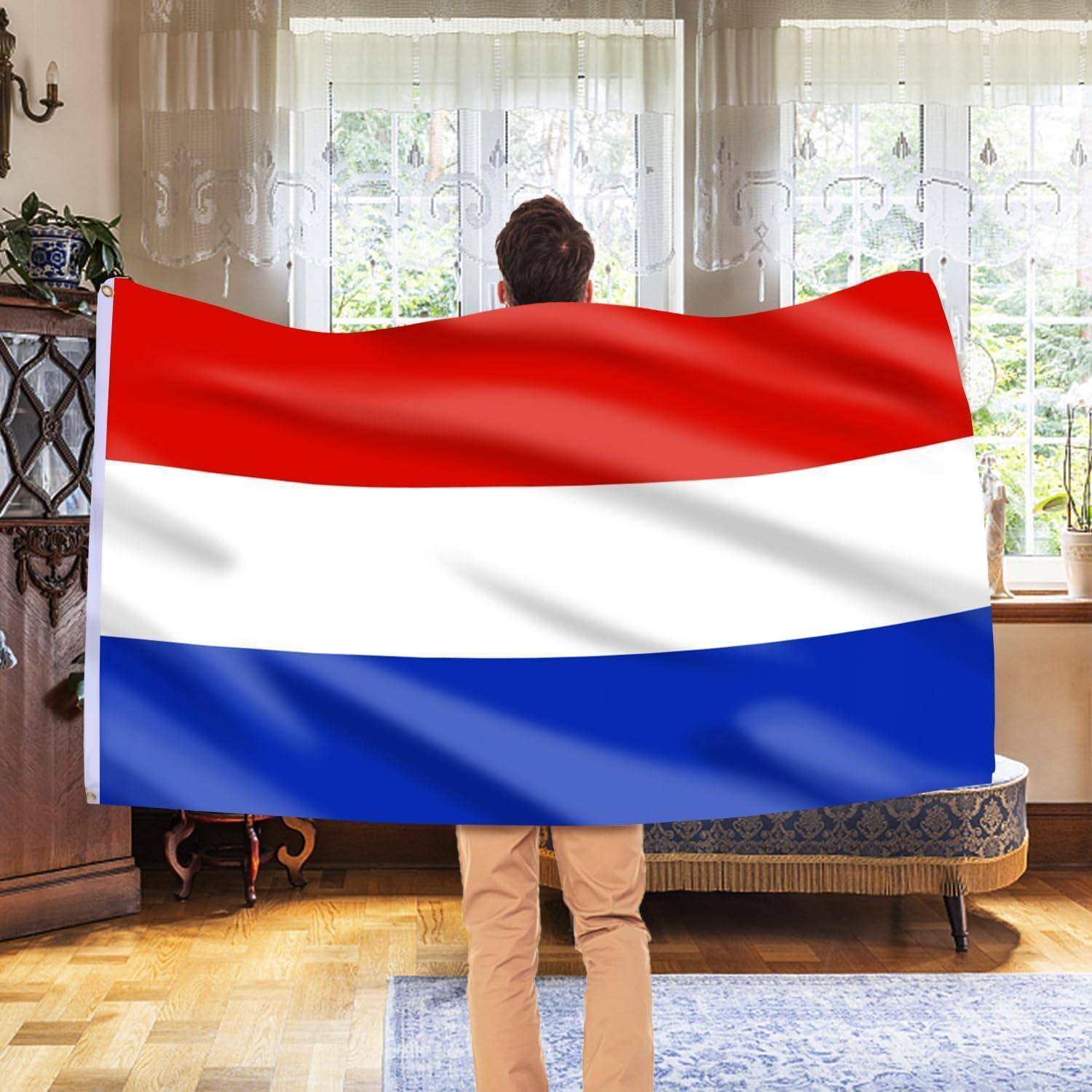 Eine Person steht in Innenräumen und hält eine große Flagge mit horizontalen Streifen in Rot, Weiß und Blau. Der Raum ist gut beleuchtet und mit dekorativen Möbeln ausgestattet.