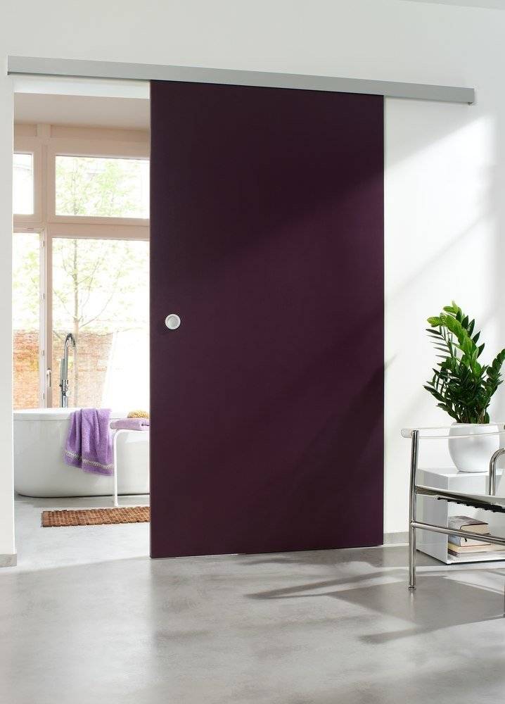 Ein modernes Badezimmer mit einer großen violetten Schiebetür. Eine Badewanne mit Handtüchern ist durch die offene Tür sichtbar. Eine Topfpflanze steht in der Nähe.