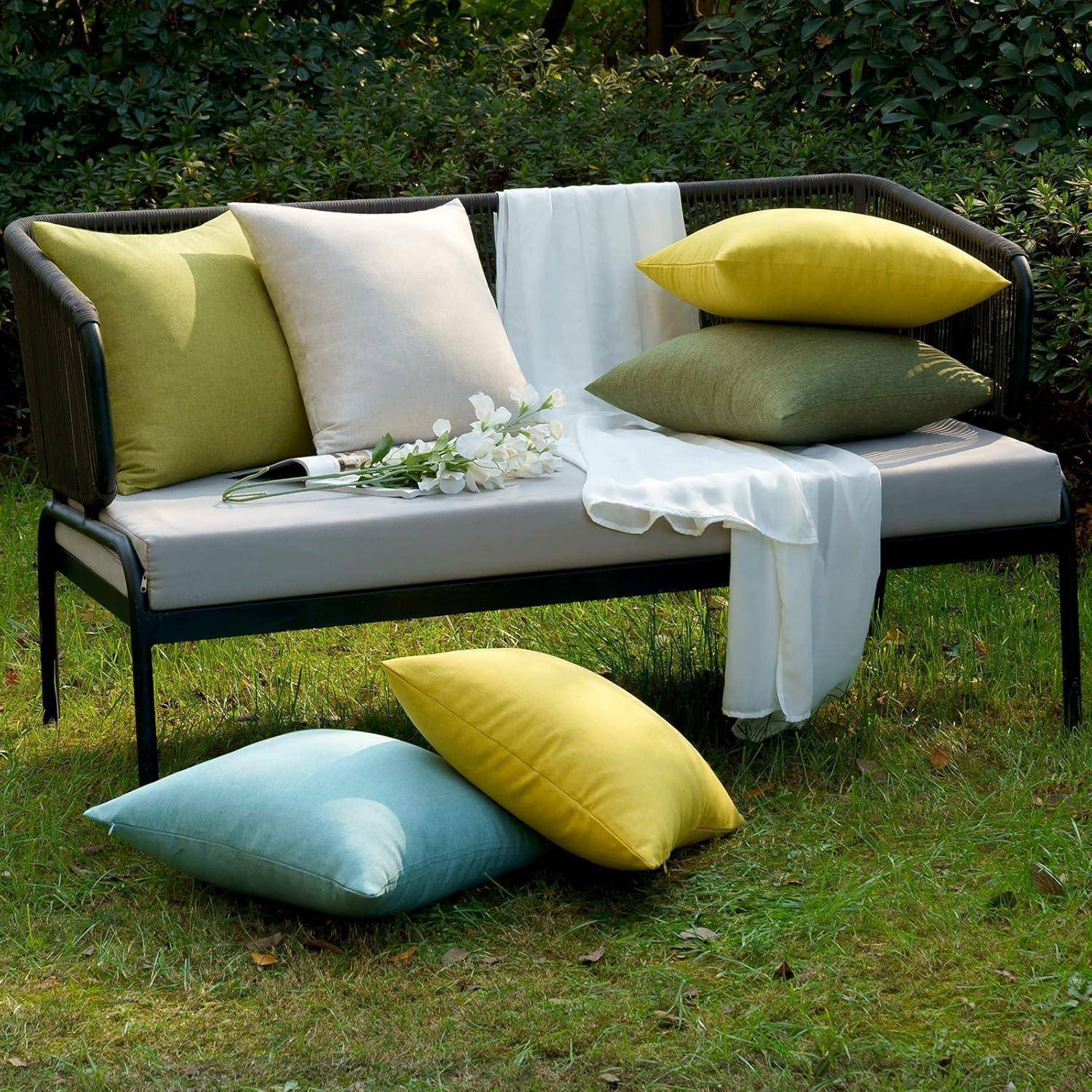 Eine Gartenbank mit einem beigen Kissen, dekoriert mit grünen, gelben und weißen Kissen. Ein weißer Blumenstrauß und ein Tuch sind darüber drapiert.
