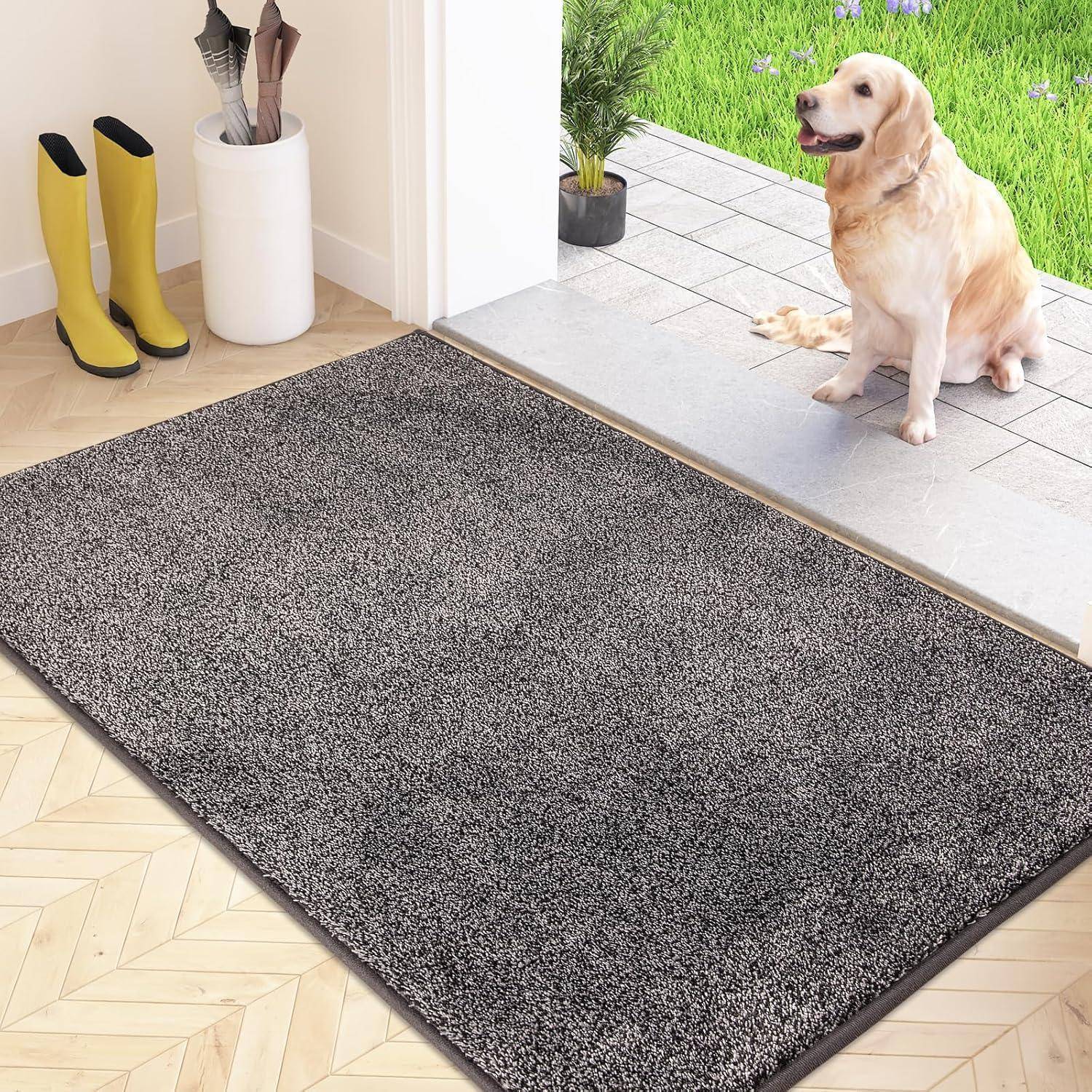 Gelbe Gummistiefel neben einer grauen Fußmatte; ein Hund sitzt draußen auf grünem Gras, sichtbar durch eine offene Tür.