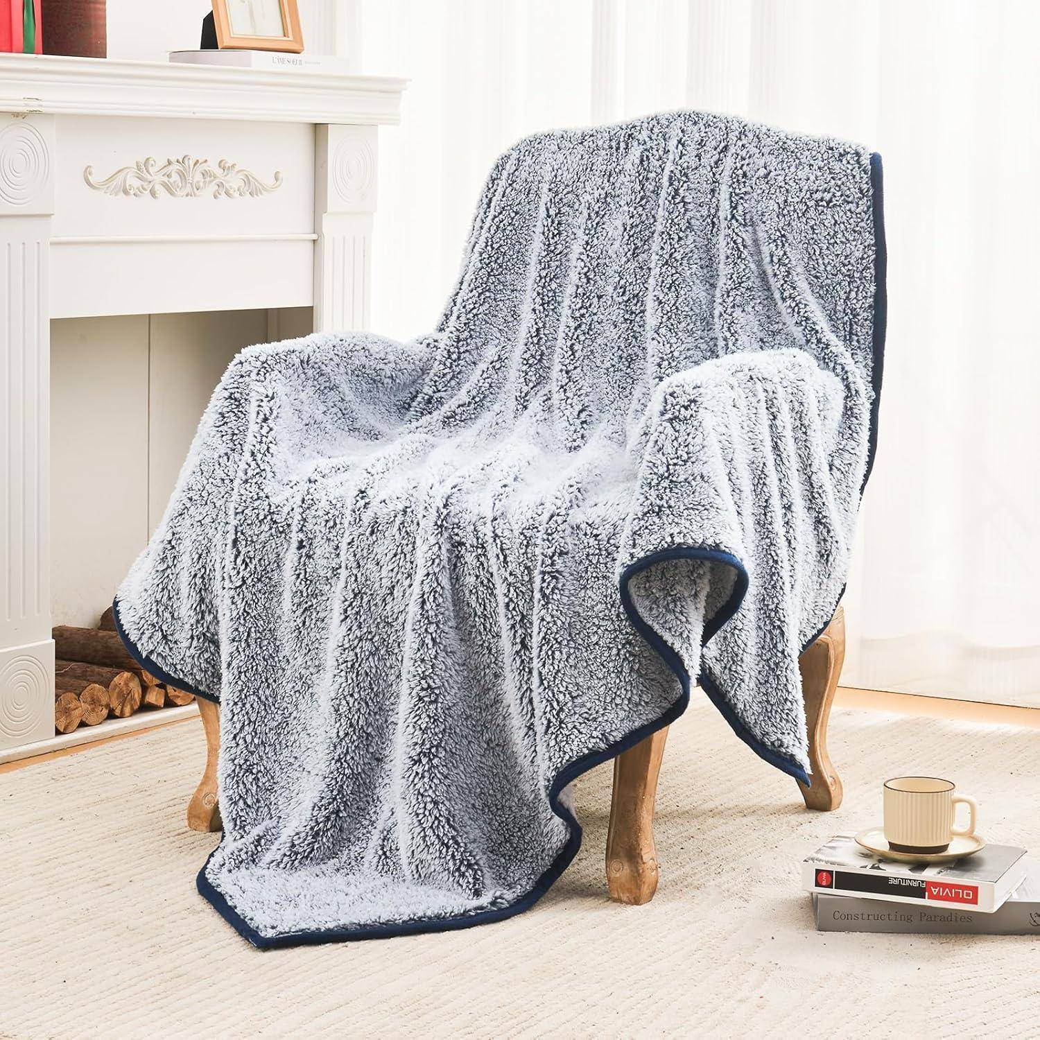Ein gemütlicher Sessel in einem hellen Wohnzimmer ist mit einer weichen, blau-weißen Plüschdecke bedeckt, neben einem kleinen Beistelltisch mit Büchern.