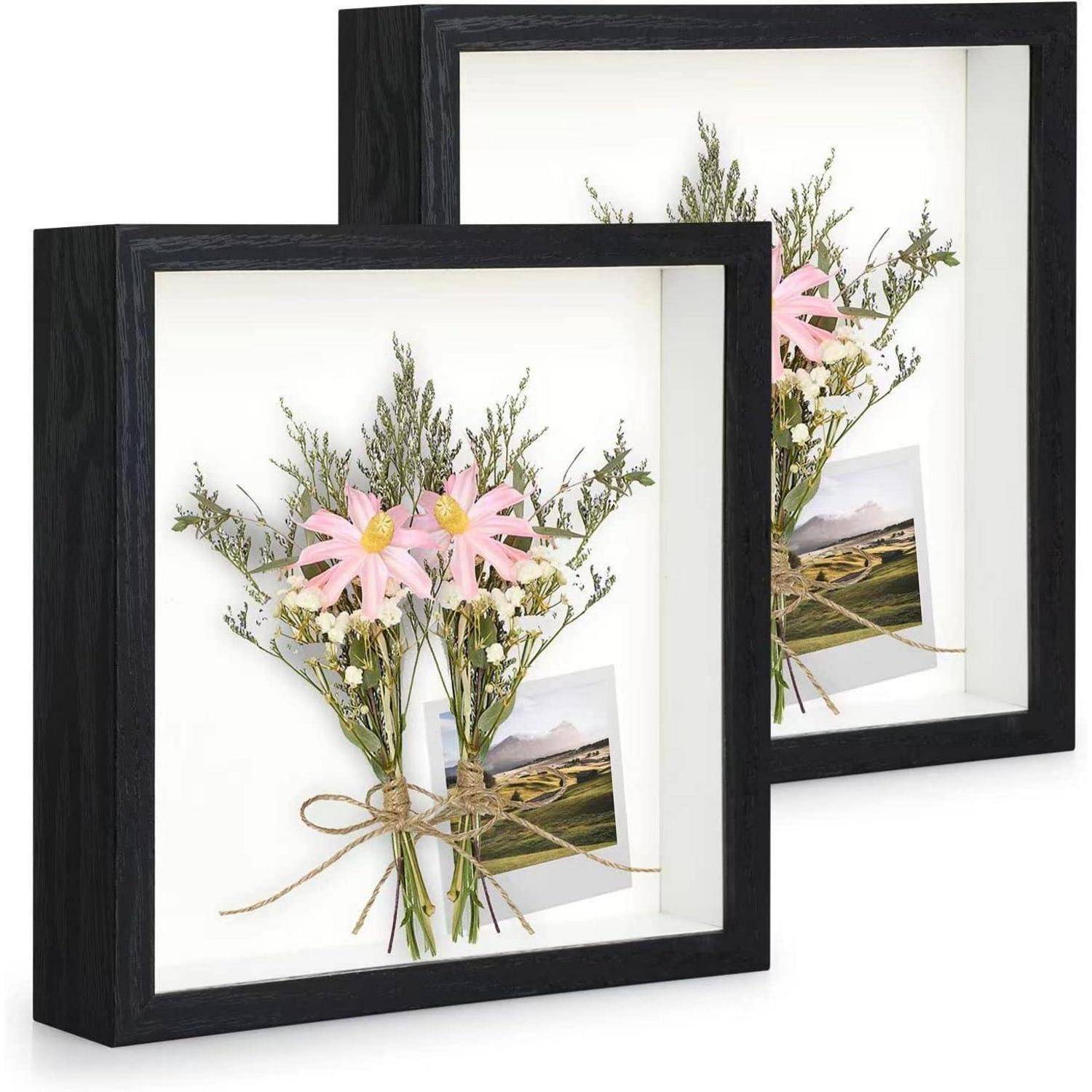 Zwei identische schwarze Schattenrahmen zeigen rosa Blumen, die mit Bindfaden zusammengebunden sind und im Hintergrund kleine eingefügte Fotos aufweisen.