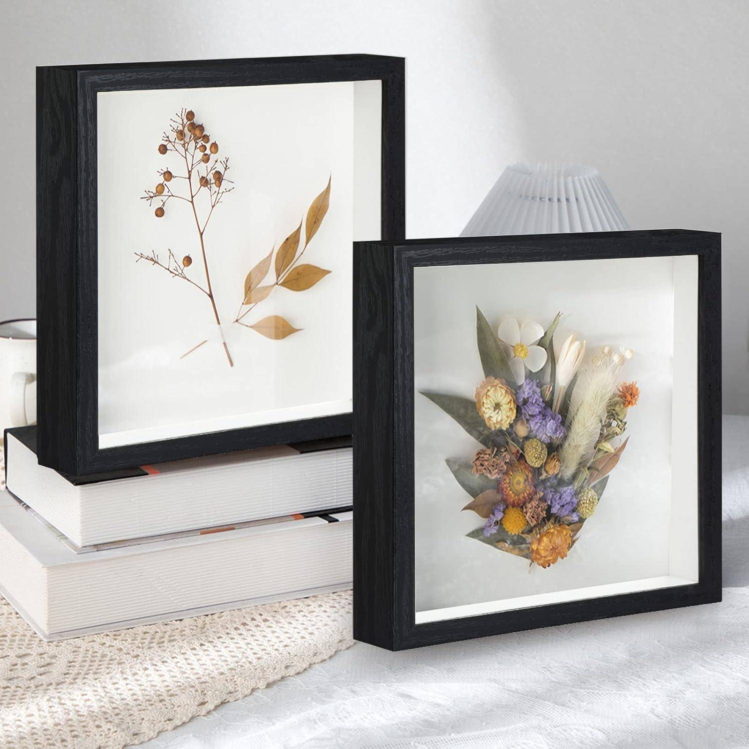 Zwei florale Kunstwerke in schwarzen Rahmen auf gestapelten Büchern; links sind getrocknete Blätter zu sehen, rechts ein farbenfroher Blumenstrauß auf weißem Hintergrund.