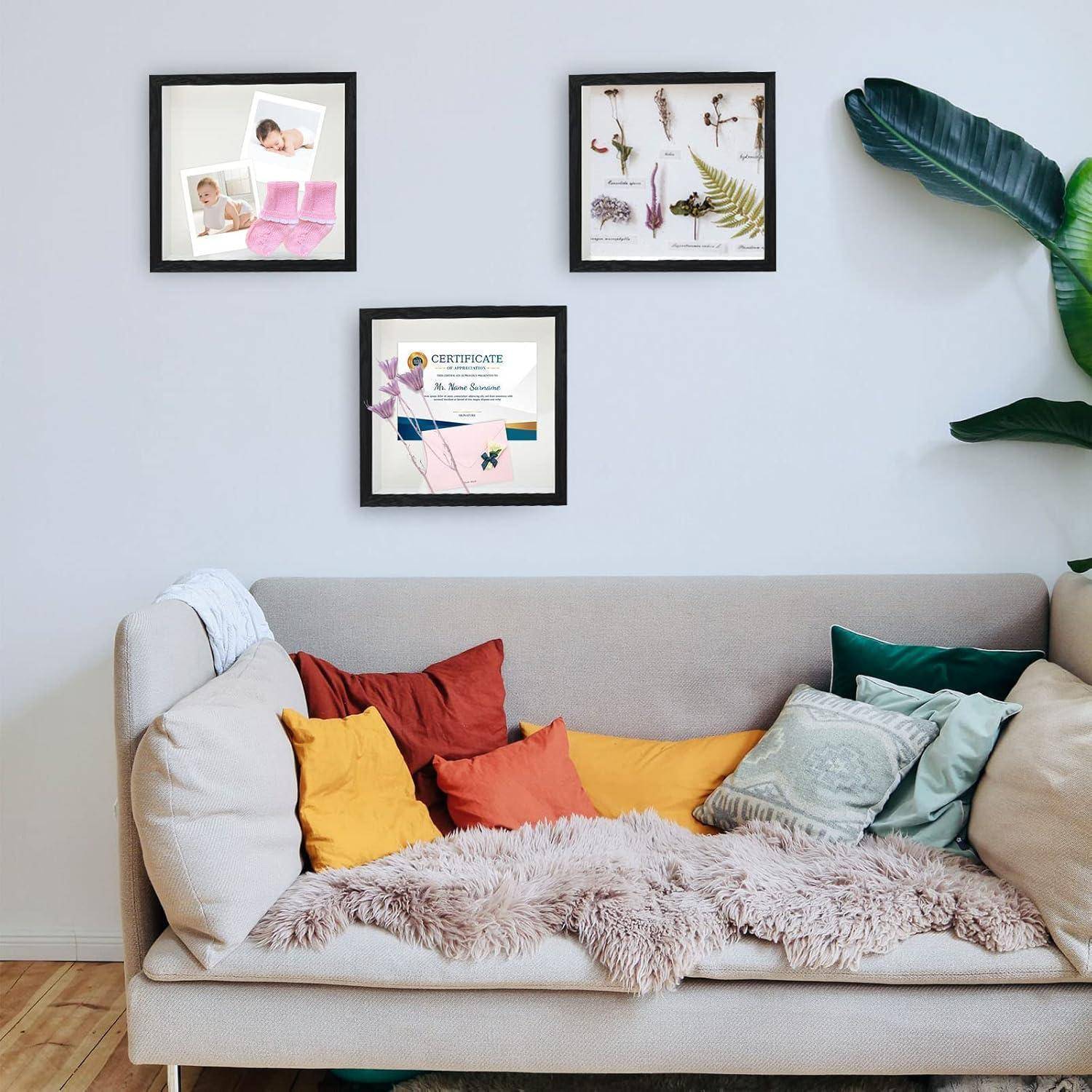 Ein gemütliches Wohnzimmer mit einem beigen Sofa, geschmückt mit bunten Kissen und einer Felldecke. Gerahmte Kunstwerke und ein Zertifikat hängen an einer weißen Wand.