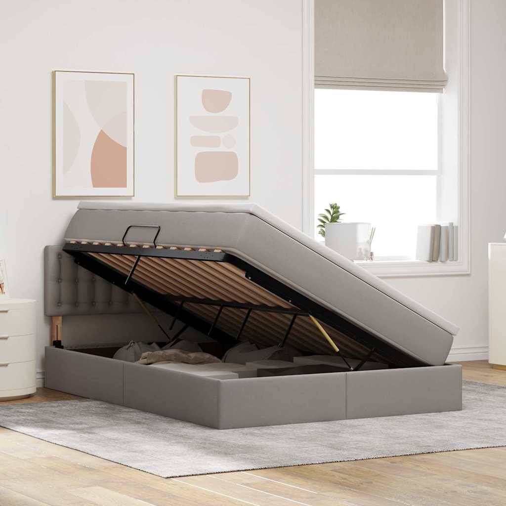 Ein grau gepolstertes Ottomanbett mit Stauraum, der offen ist und Gegenstände im Inneren zeigt. Der Raum hat minimalistische Dekoration mit abstrakter Kunst an den Wänden.