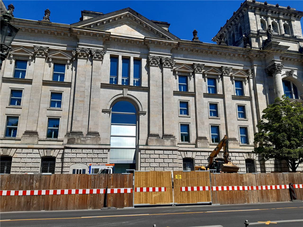 Ein großes historisches Gebäude während der Renovierung, umgeben von einem Holzzaun und Bauausrüstung, was laufende Restaurierungsarbeiten andeutet.
