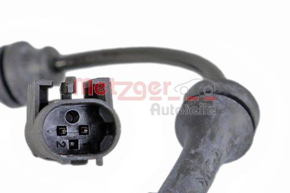 Nahaufnahme eines Autosensors mit elektrischem Anschluss-Stecker, der zwei mit '1' und '2' beschriftete Stifte aufweist. Im Hintergrund sind Teile der Verkabelung zu sehen.