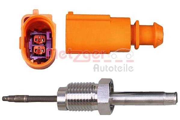 Orangefarbener Stecker mit sichtbaren Anschlüssen neben einer Metallsonde, mit 'Metzger Autoteile' in verschwommenem rotem Text im Hintergrund beschriftet.