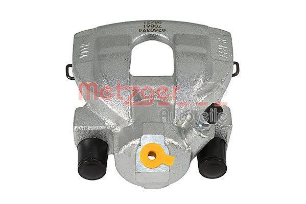 Eine silberne Bremssattel mit einer zentralen Öffnung, zwei schwarzen Zylindern und einer gelben Plastikkappe am unteren Ende.