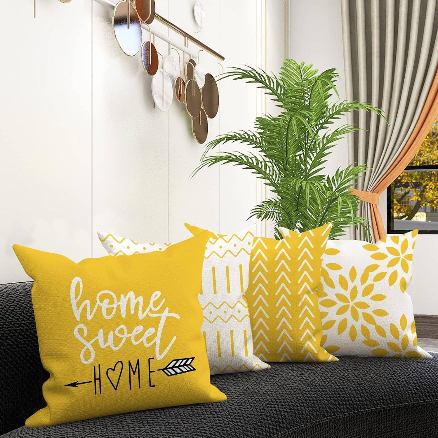Ein gemütliches Wohnzimmer mit einem schwarzen Sofa, geschmückt mit vier dekorativen gelben und weißen Kissen. Ein Kissen trägt die Aufschrift „Zuhause süßes Zuhause