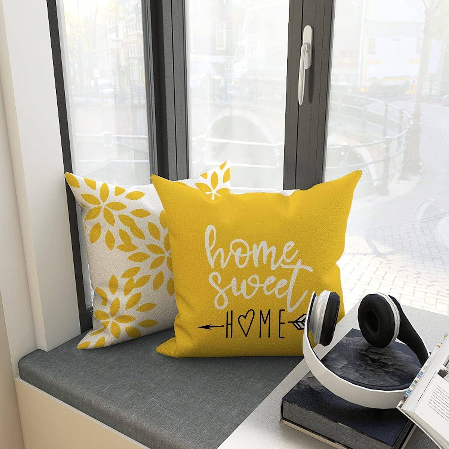 Zwei dekorative Kissen auf einer Fensterbank, eines gelb mit dem Schriftzug 'Home Sweet Home', daneben Kopfhörer und Bücher, mit Blick auf eine Stadtlandschaft.