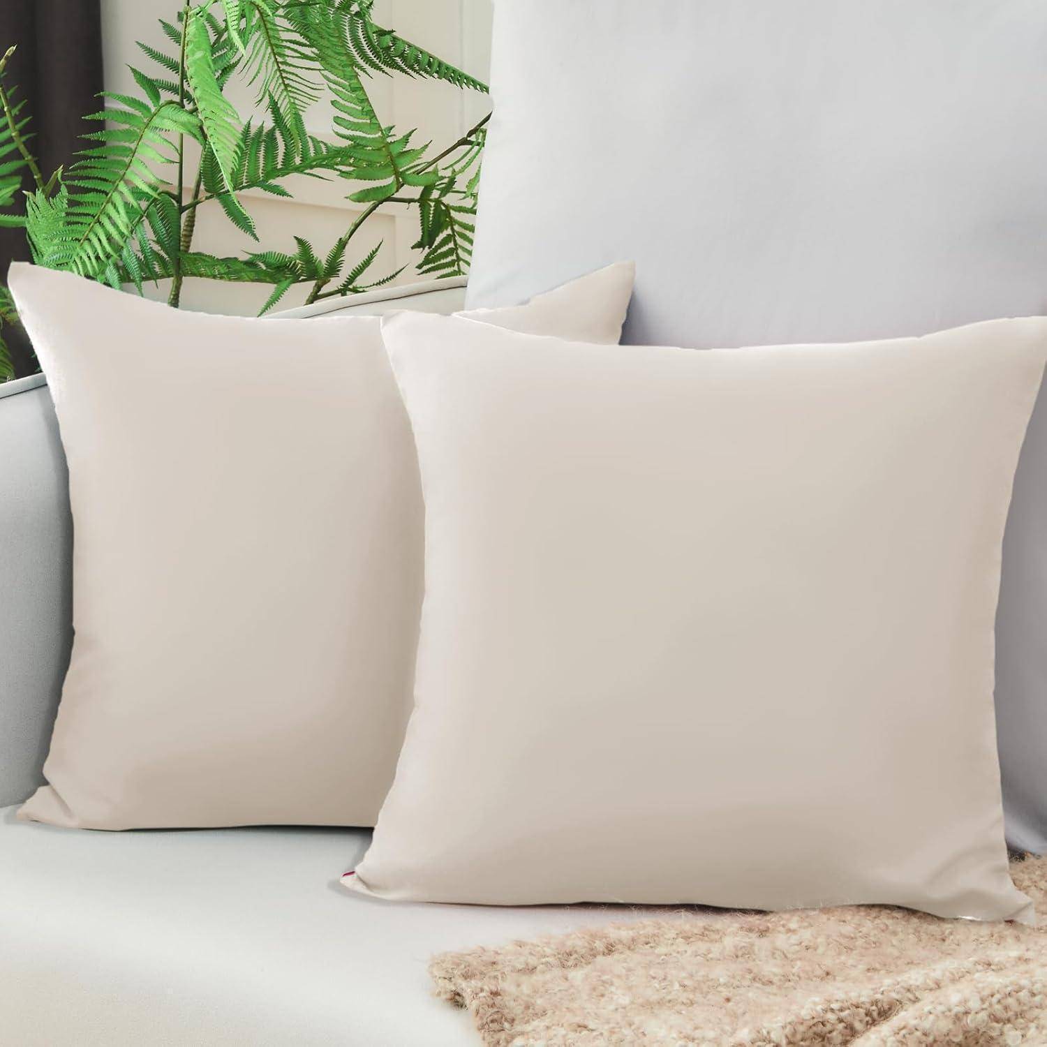 Zwei weiße Kissen auf einem hellgefärbten Sofa mit grünen Pflanzen im Hintergrund, die eine ruhige und gemütliche Atmosphäre vermitteln.