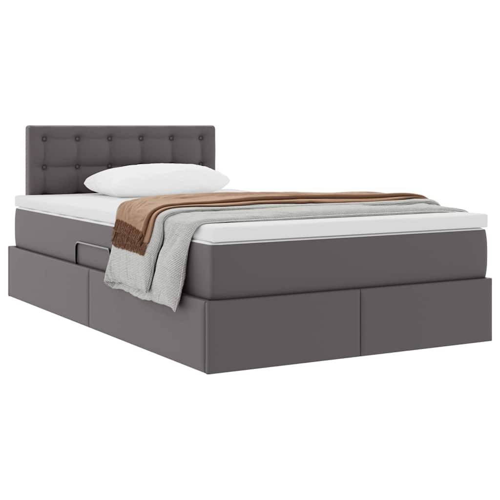 Ein graues gepolstertes Bett mit einer gesteppten Kopfstütze, weißer Matratze, weißem Kissen und mehreren Decken in Braun- und Grautönen.