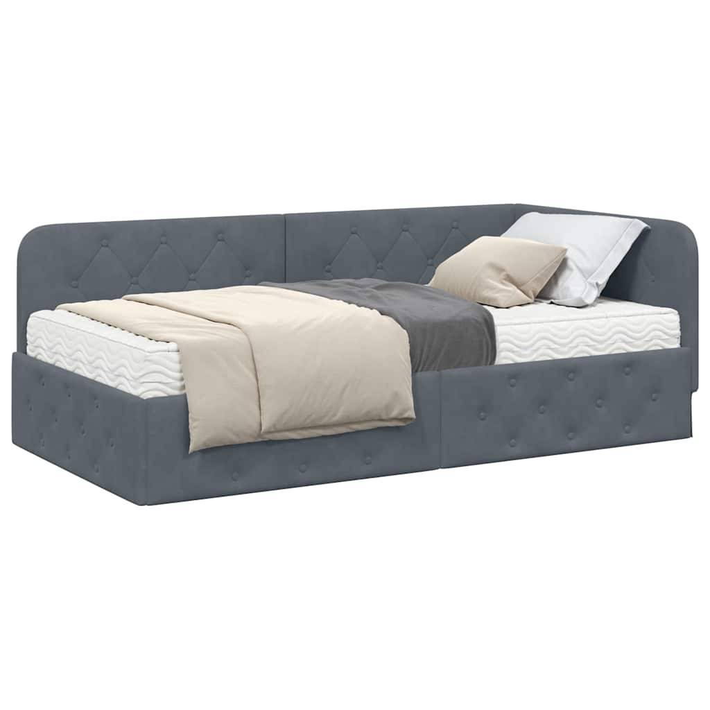Ein grau gepolstertes Tagesbett mit Knopfheftung verfügt über eine weiße Matratze, graue und beige Bettwäsche und ein weißes Kissen, das in einer Ecke platziert ist.