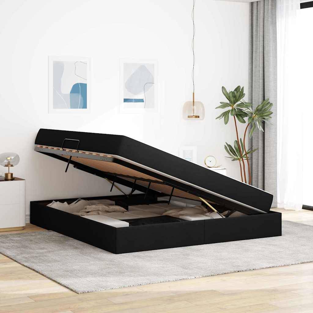 Ein modernes Schlafzimmer zeigt ein schwarzes Stahlbett mit teilweise offenem Deckel, das Stauraum darunter sichtbar macht. Das Zimmer hat helle Wände, zwei abstrakte Kunstwerke, eine Pflanze und eine Hängeleuchte.