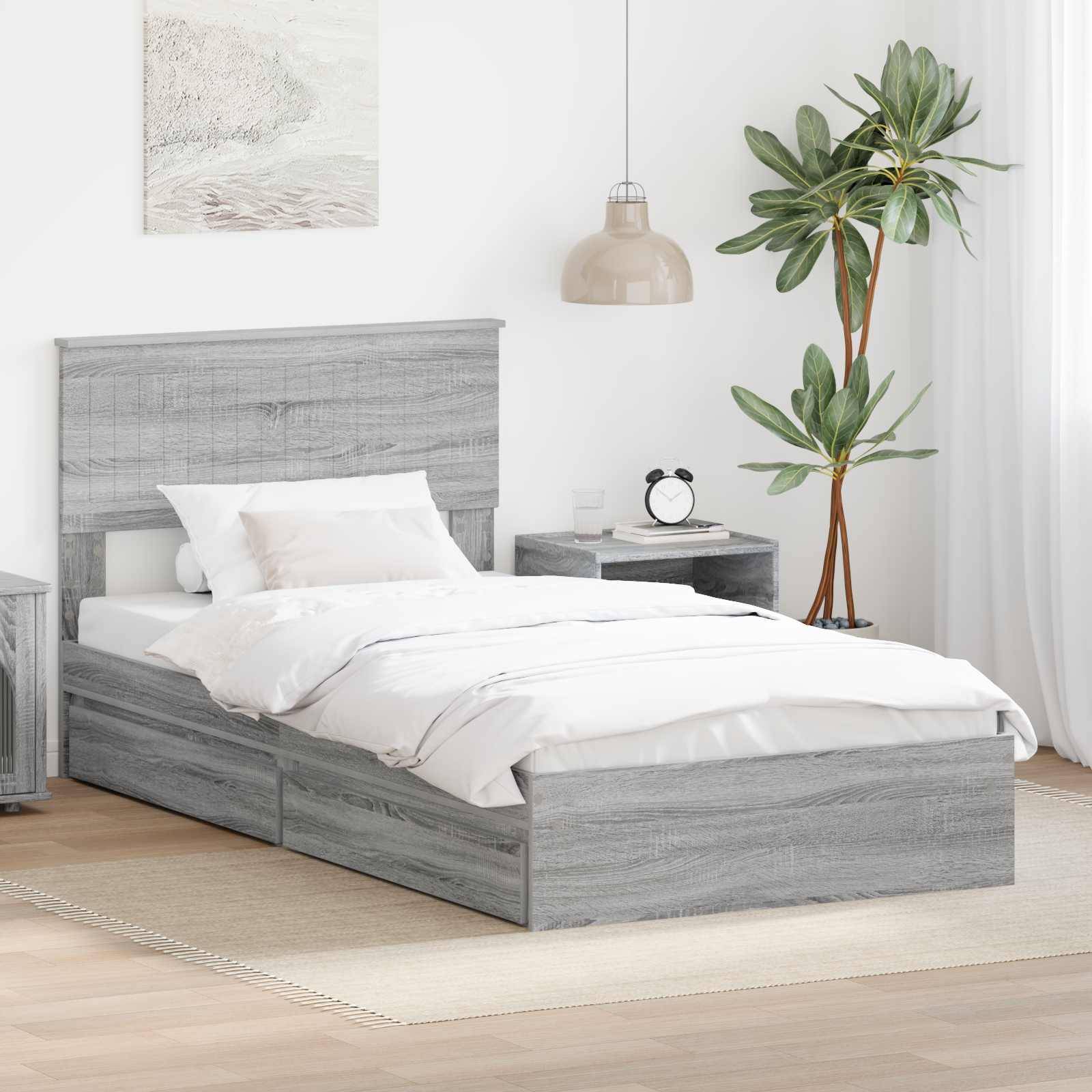 Ein modernes Schlafzimmer mit einem grauen Holzbett, weißer Bettwäsche, Nachttisch, Lampe und einer grünen Topfpflanze in einer hellen, minimalistischen Umgebung.