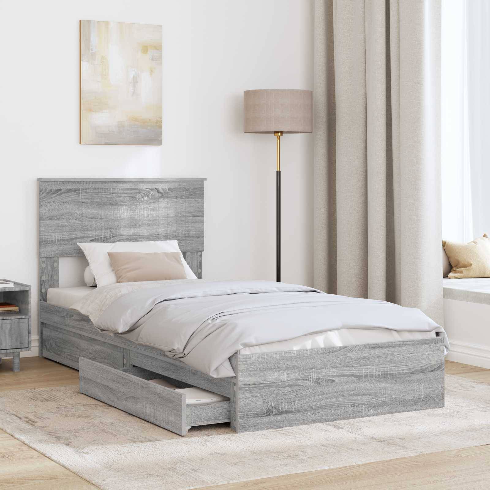 Ein Schlafzimmer ist mit einem grauen Holzbett mit Schubladen darunter, einem passenden Nachttisch, einer beigen Lampe und einer Fensterbank mit Kissen ausgestattet.