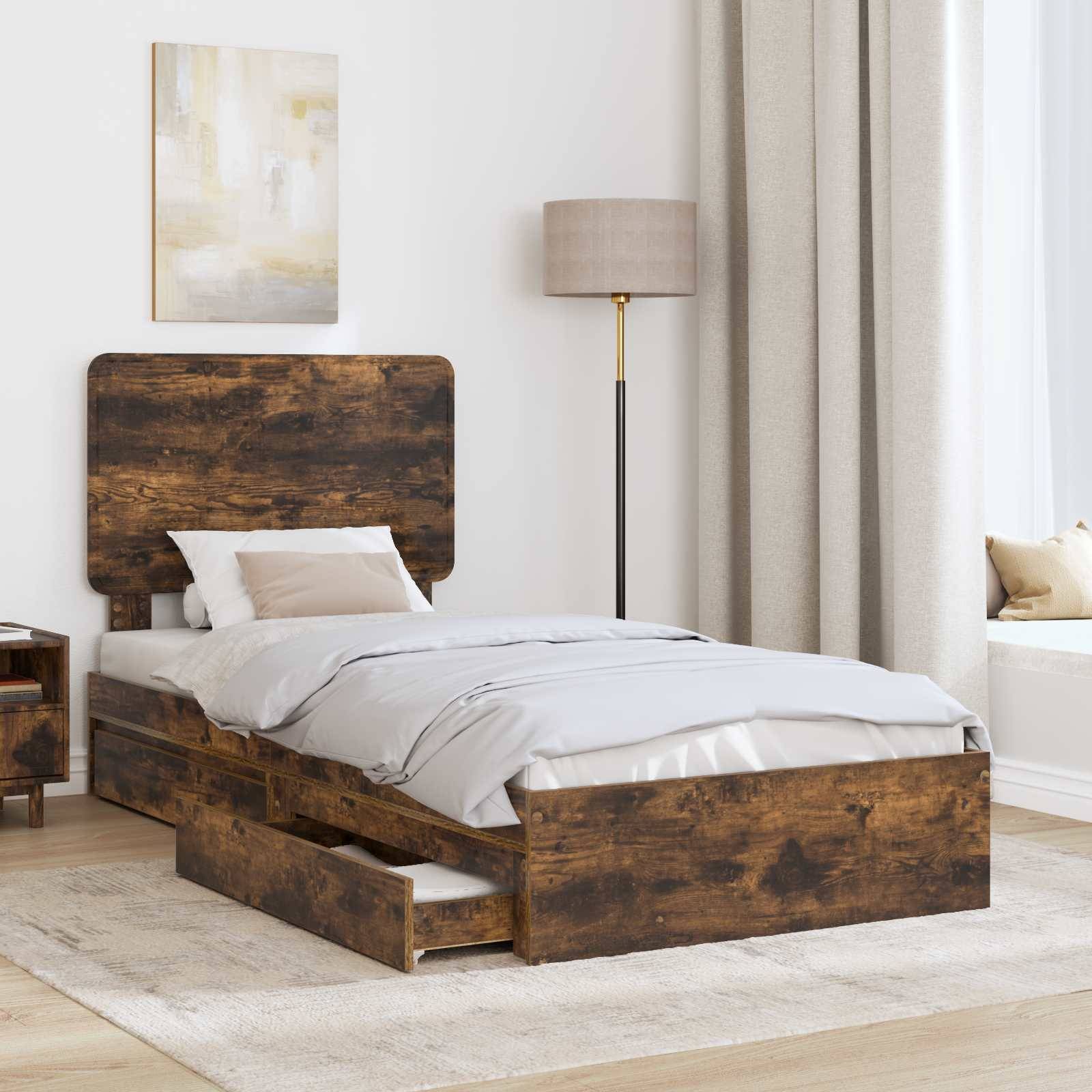 Ein rustikales Holzbett mit weiß-grauer Bettwäsche, zwei offene Schubladen darunter. In der Nähe ein hölzerner Nachttisch und eine hohe Stehlampe.