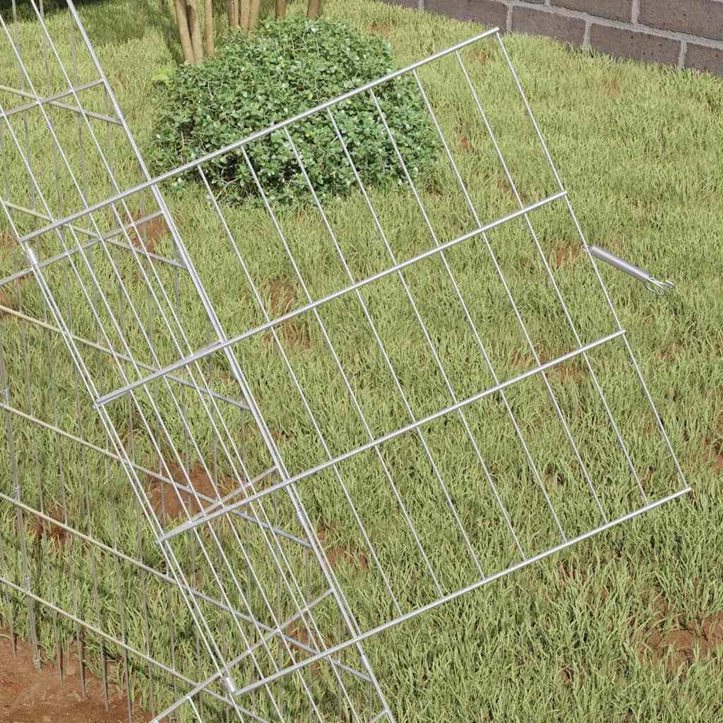 Ein Metallzaunpaneel liegt auf Gras, leicht geneigt, neben einem Baum und einer Ziegelwand.