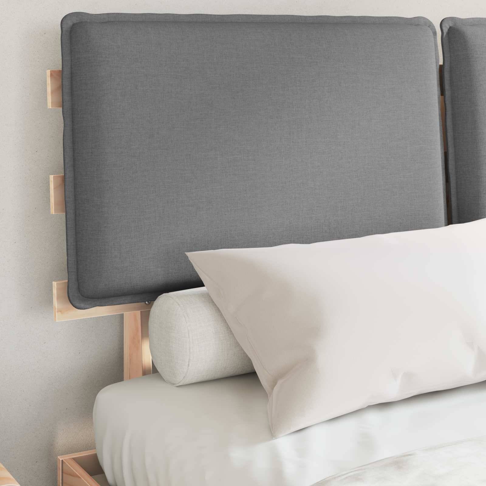 Ein ordentlich gemachtes Bett mit einem grauen Kopfteil, weißem Kissen und hellgrauem Nackenrollo, vor einer hellgefärbten Wand.