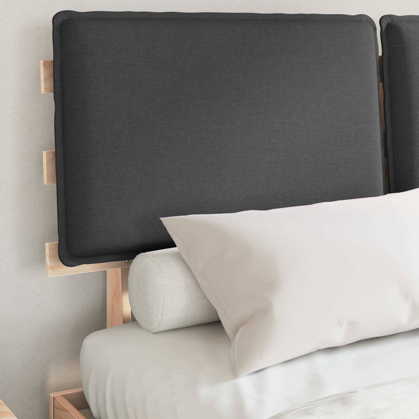 Ein ordentlich gemachtes Bett mit einem grauen gepolsterten Kopfteil, weißem Kissen und einem aufgerollten Kissen vor einer hellen Wand.